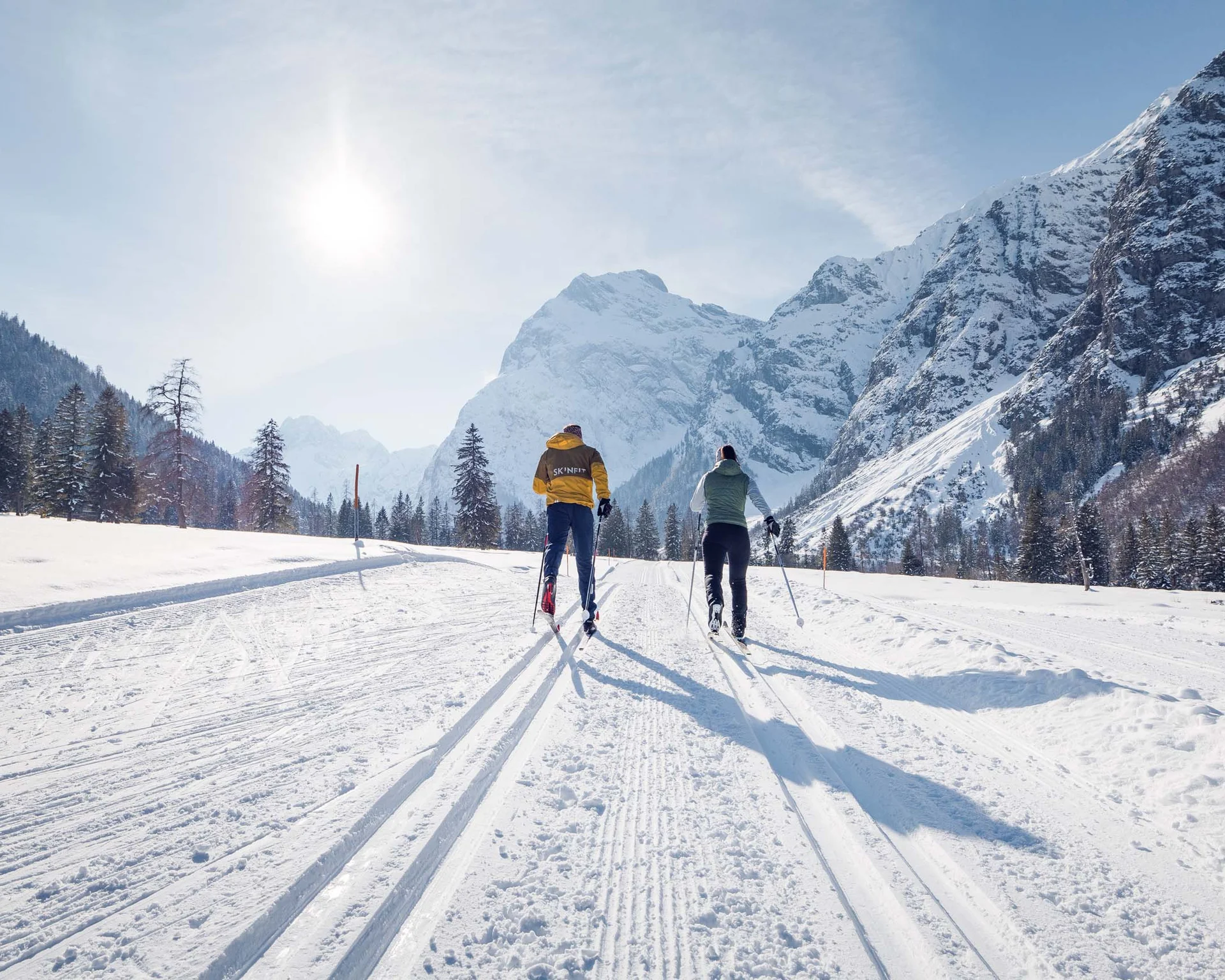 Zwei Menschen beim Langlaufen auf verschneiter Bergstrecke unter Sonnenschein
