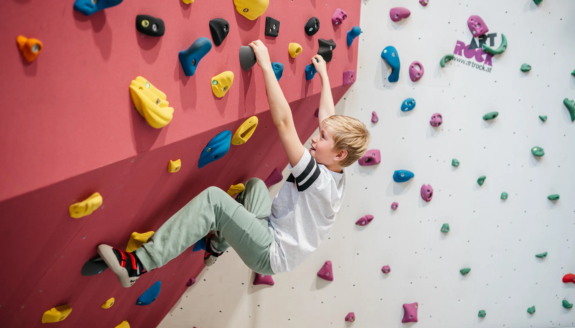 Junge klettert an bunten Griffen an einer Kletterwand in der Halle