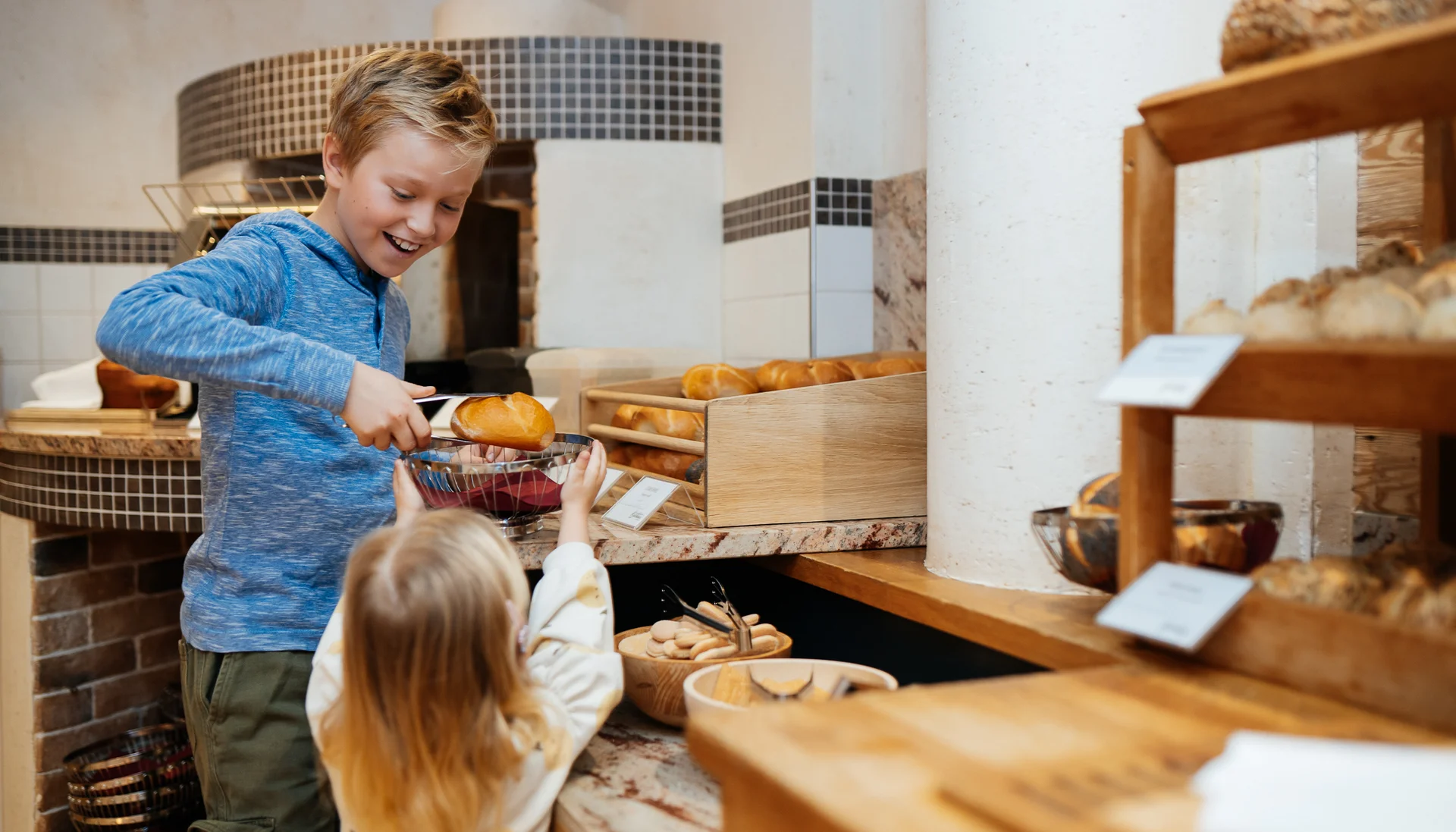 Junge gibt Mädchen in Bäckerei mit Zange frisches Brötchen