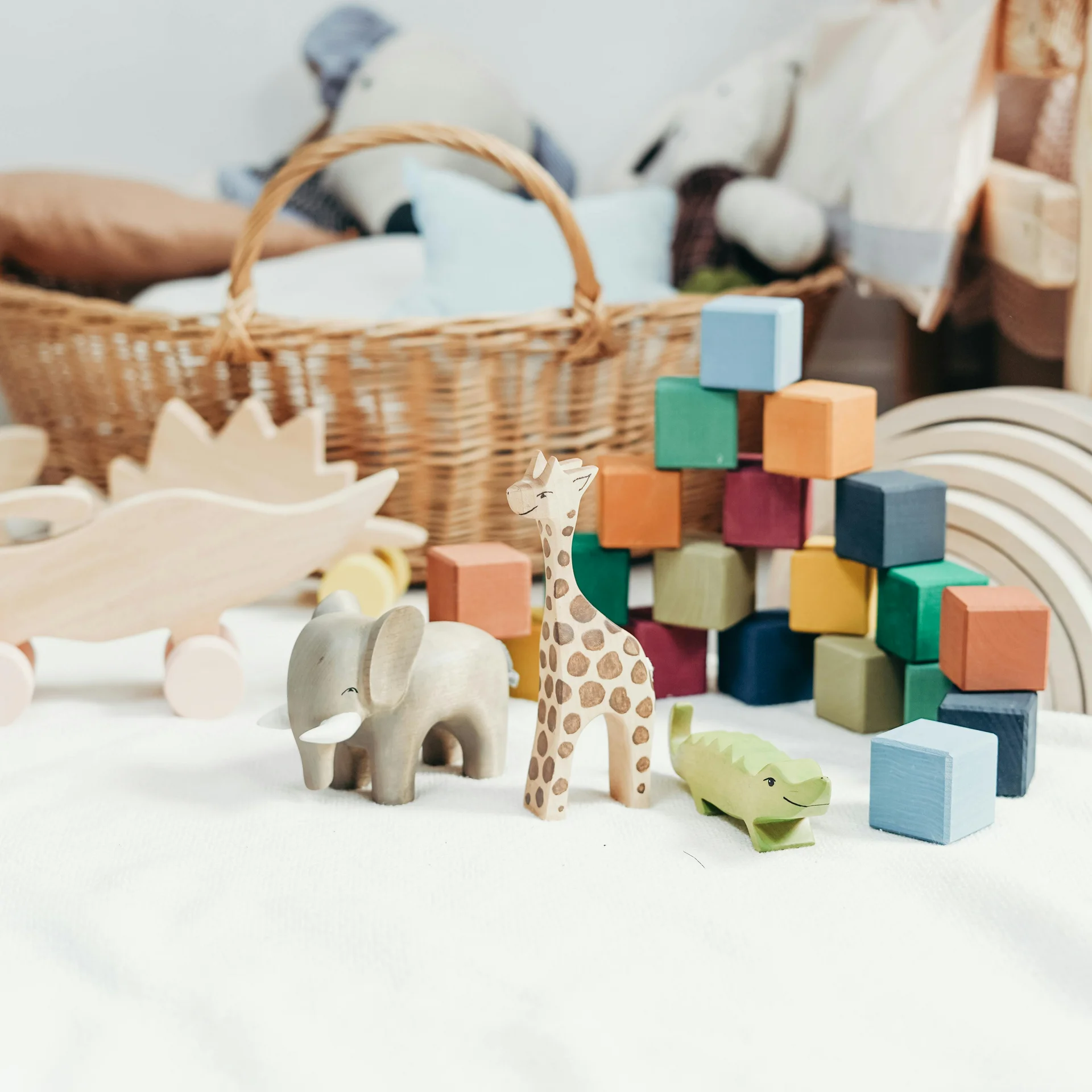 Wooden toy animals and colorful blocks on white carpet with basket and wall decor