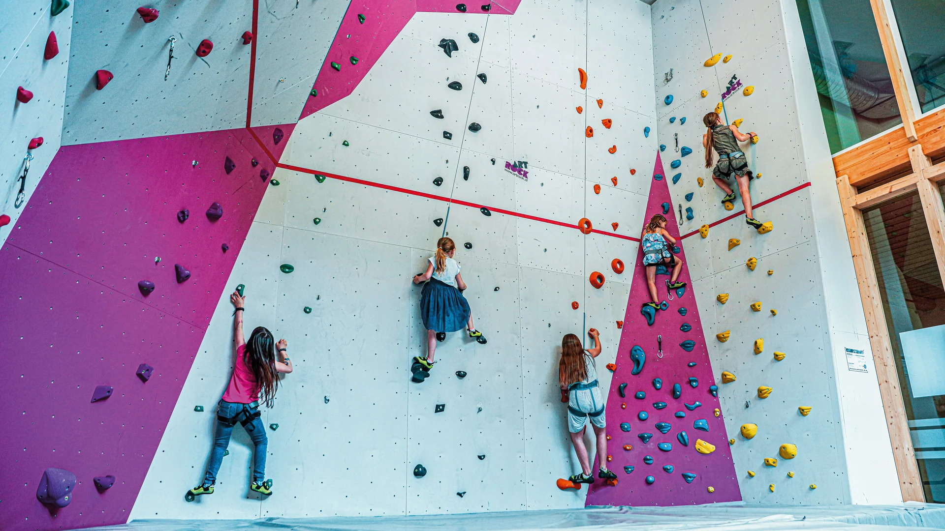 Kinder klettern an einer bunten Indoor-Kletterwand in einer Halle