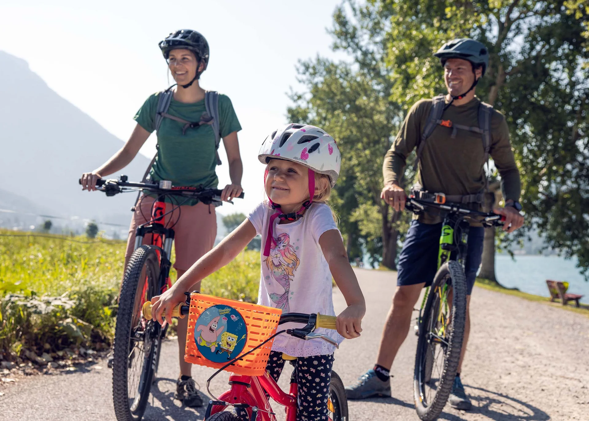 Familie mit Kind auf Fahrradtour in sonniger Landschaft mit Bergen und See