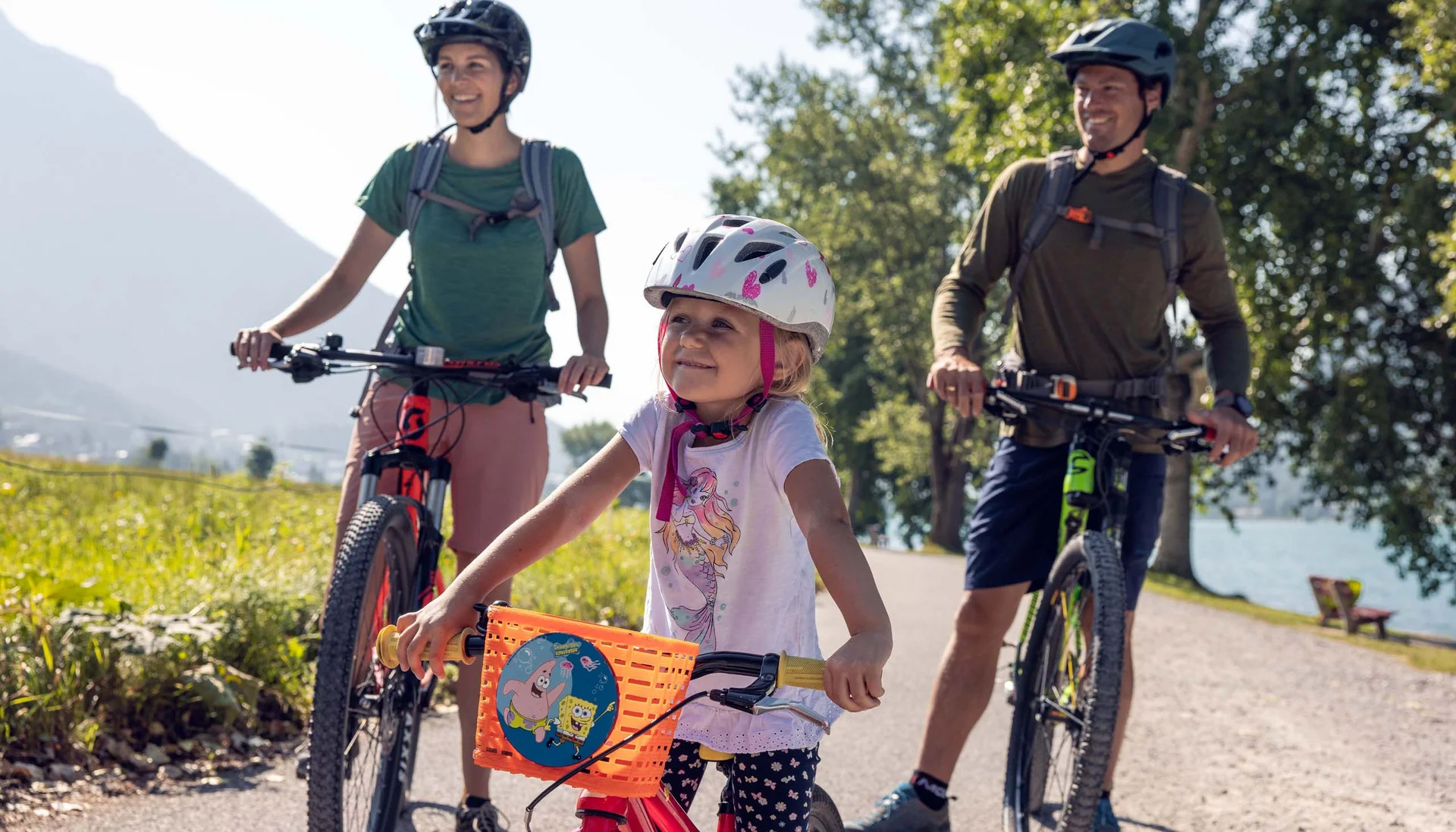 Familie mit Kind auf Fahrradtour in sonniger Landschaft mit Bergen und See