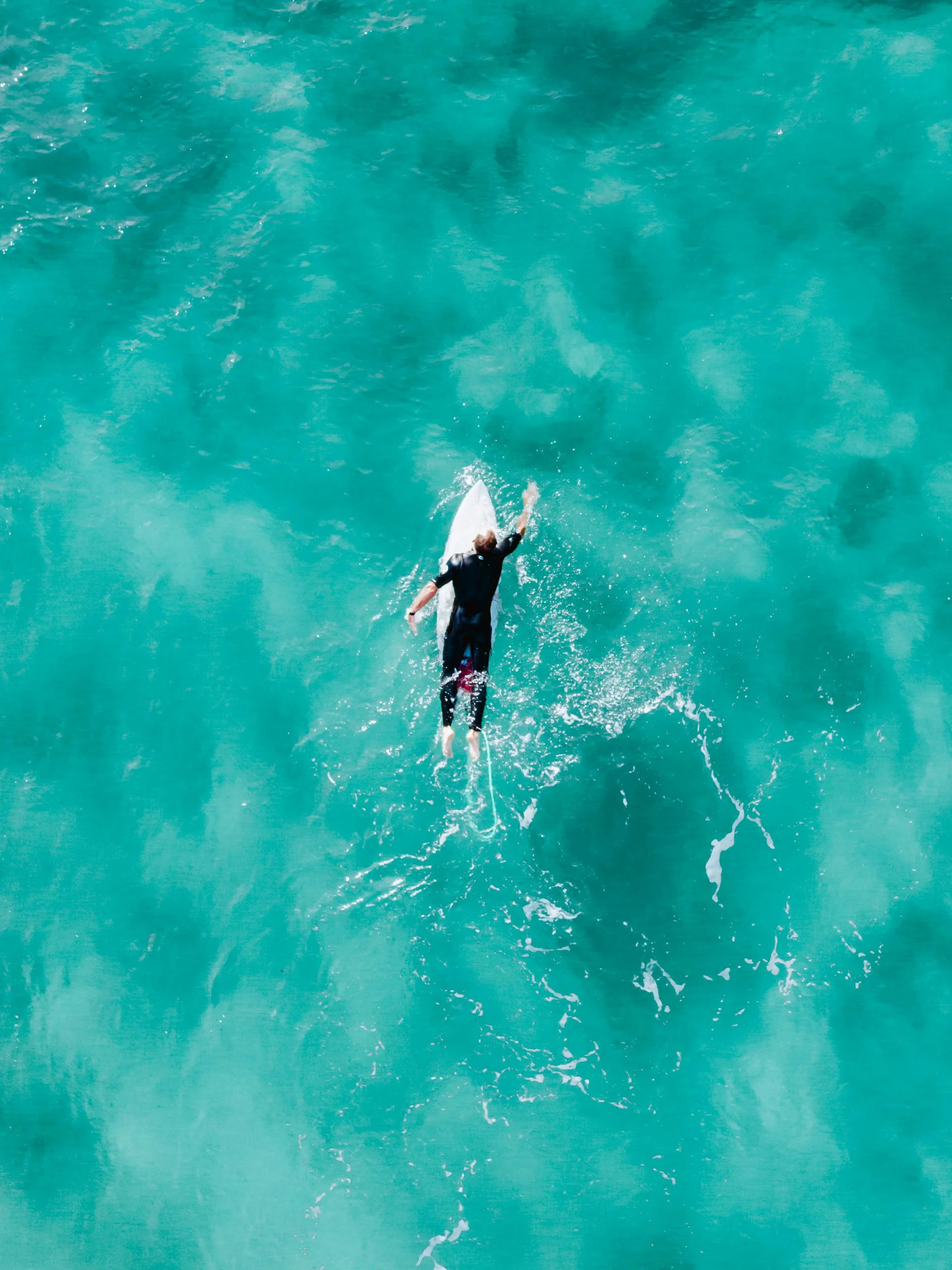 Ein Surfer paddelt auf einem Surfbrett im klaren türkisfarbenen Meer