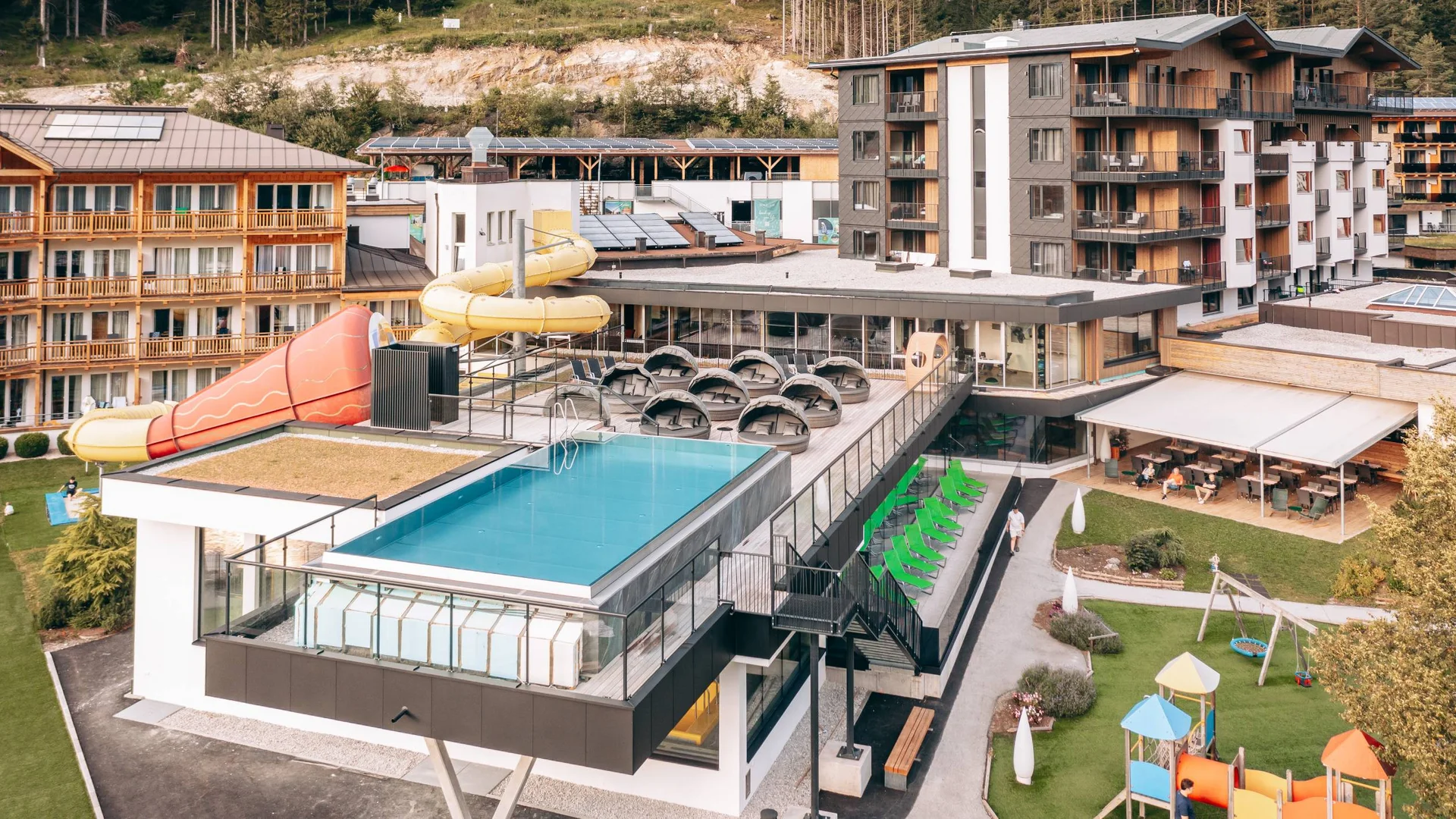 Hotel mit Außenpool, Wasserrutsche und Spielplatz in einer Berglandschaft