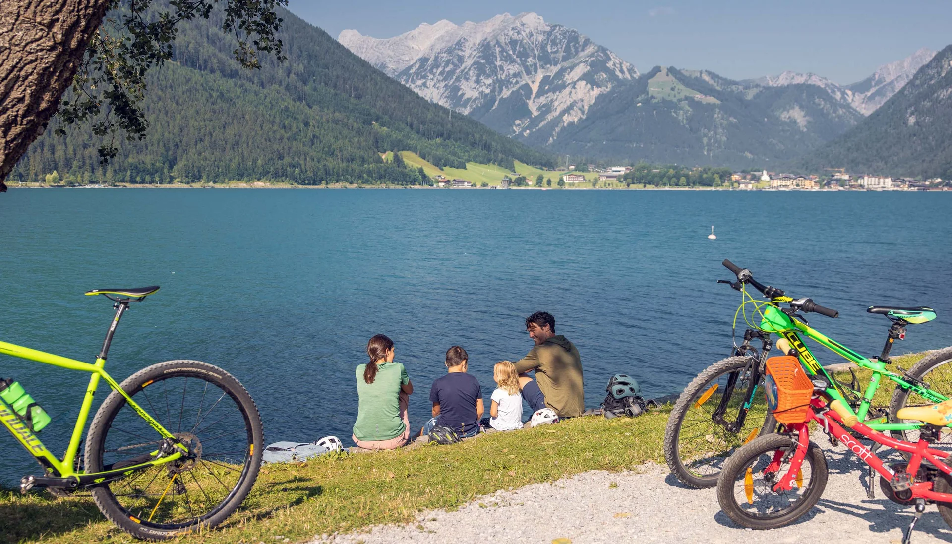 Familie mit Fahrrädern am See vor Alpenpanorama bei Sonnenschein