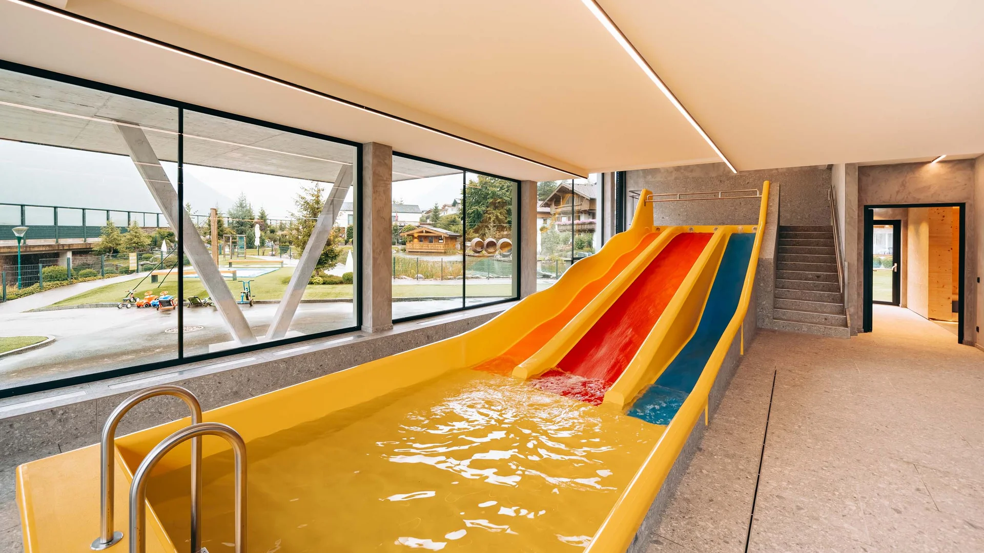 Innenschwimmbad mit drei bunten Wasserrutschen und großen Fenstern zum Garten