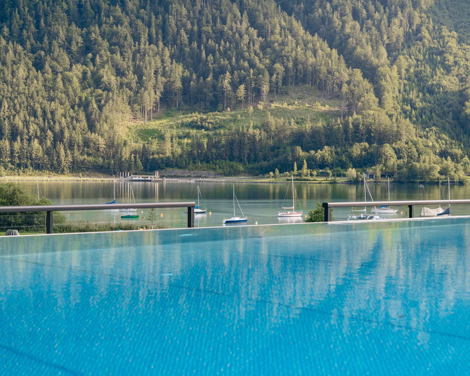 Blick auf See mit Segelbooten und bewaldeten Bergen im Hintergrund