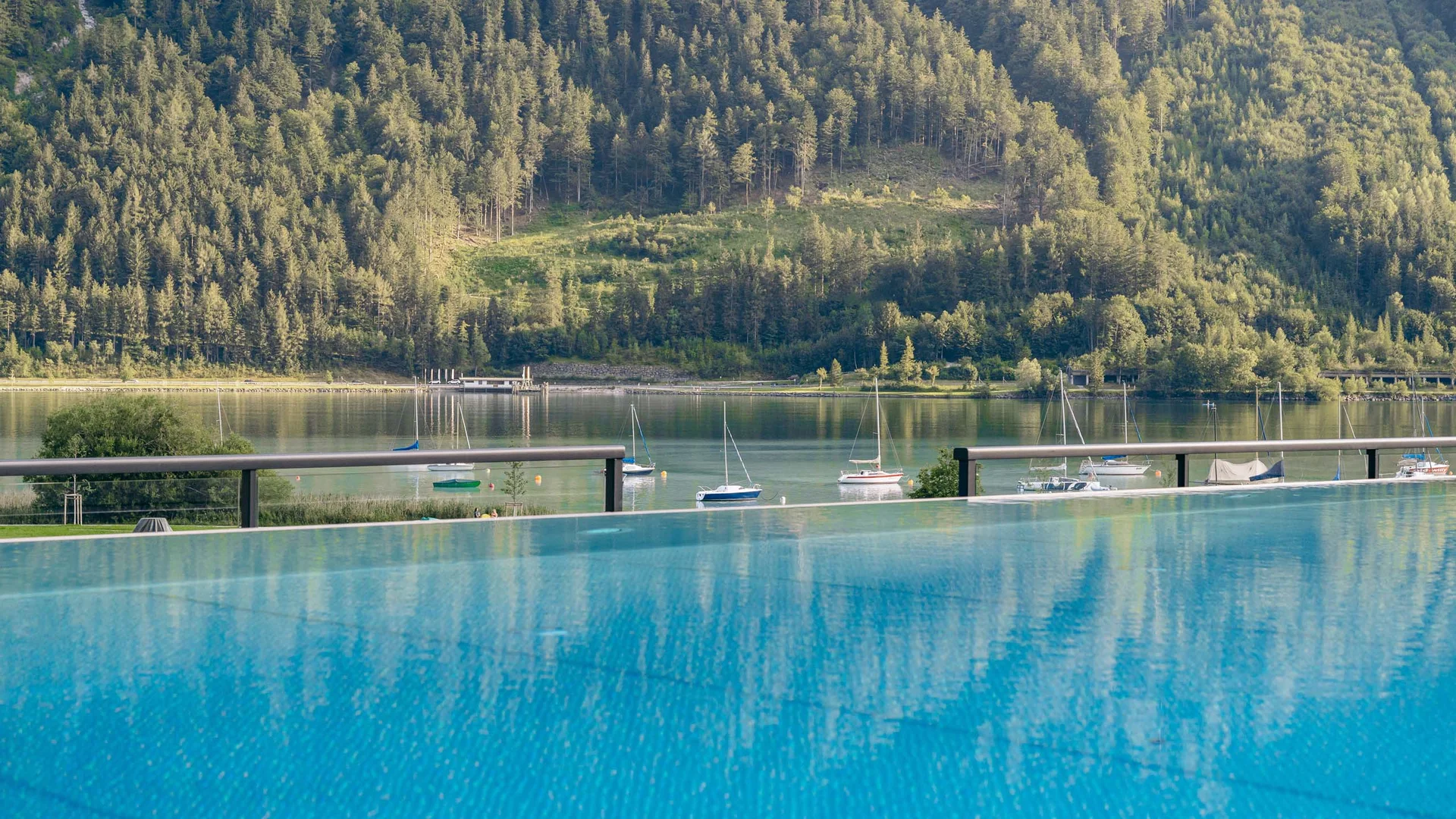 Blick auf See mit Segelbooten und bewaldeten Bergen im Hintergrund