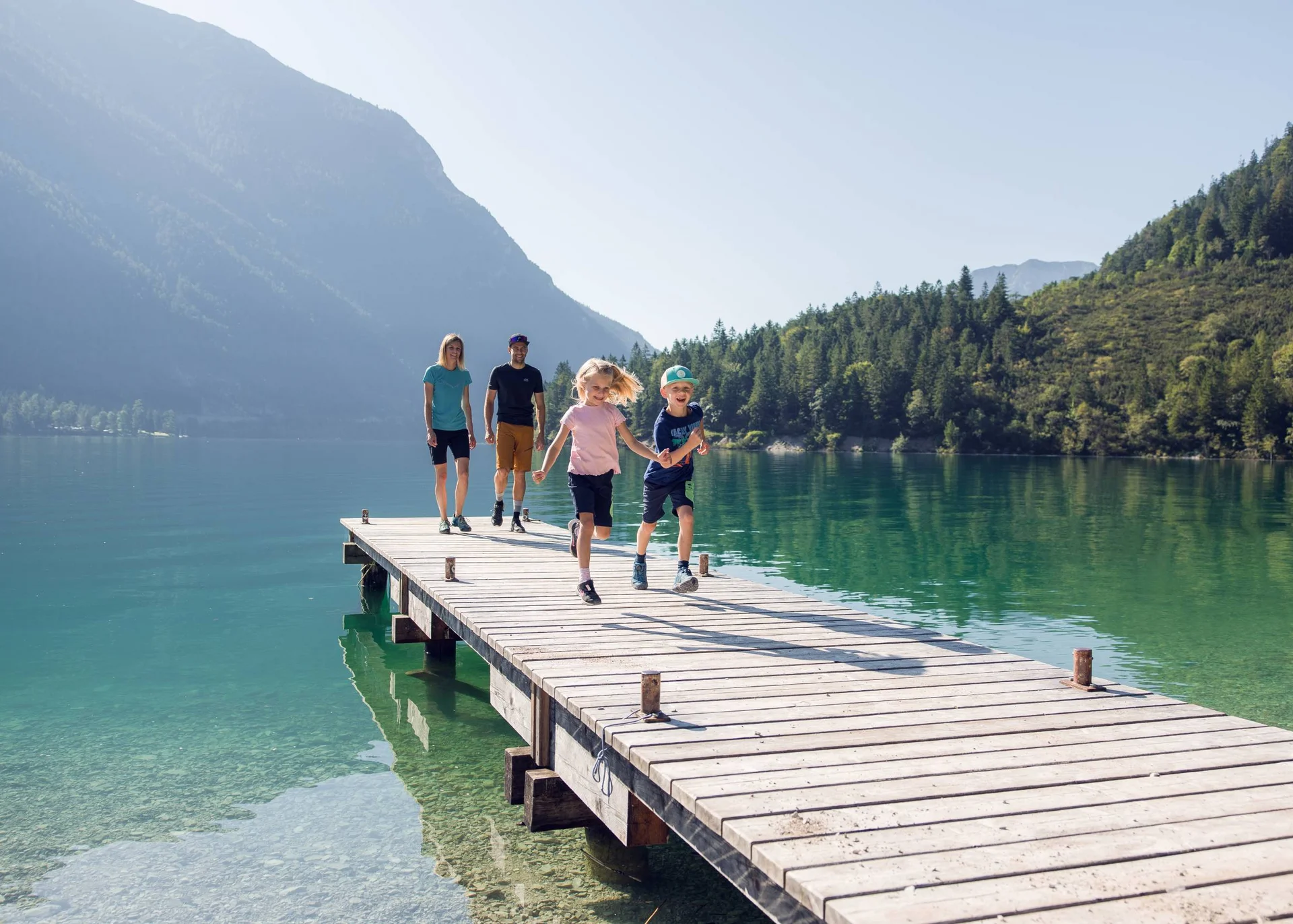 Family with two kids walking on a dock over a mountain lake on a sunny day