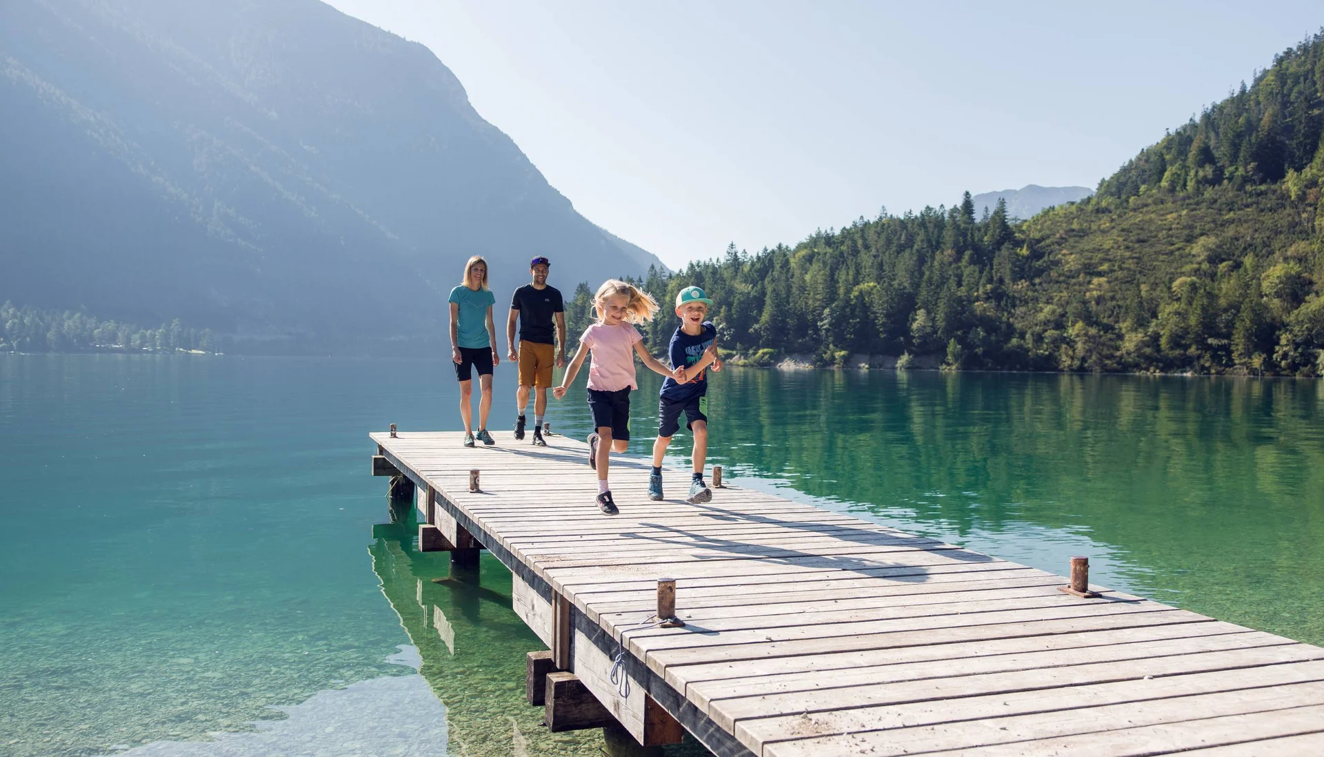 Family with two kids walking on a dock over a mountain lake on a sunny day