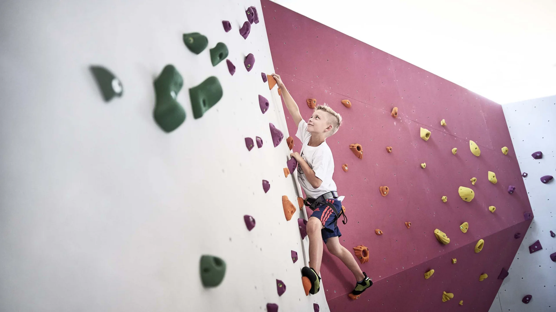 Junge beim Klettern an einer bunten Kletterwand in der Halle