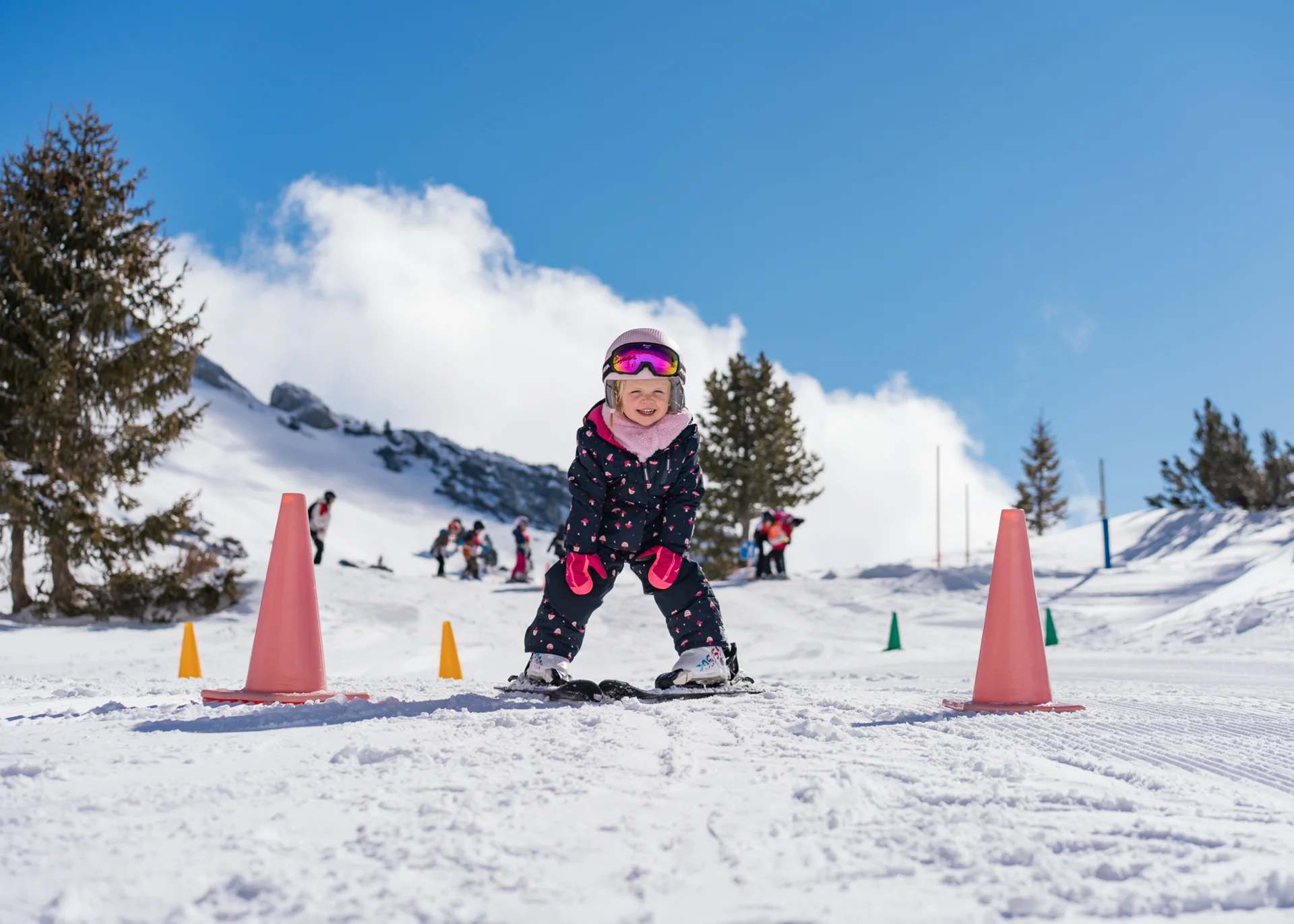 Kleines Kind lernt Skifahren zwischen orangen Hütchen im Schnee bei Sonnenschein