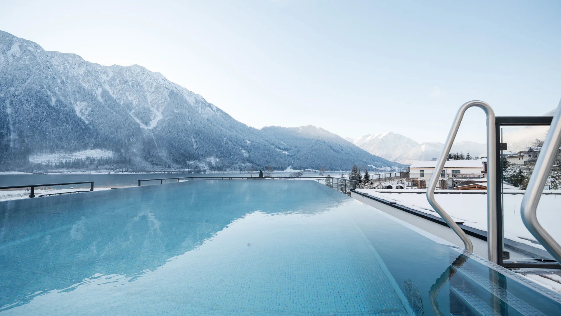 Holiday at a family spa hotel in Austria Infinity pool overlooking snow-covered mountains and a lake under clear sky
