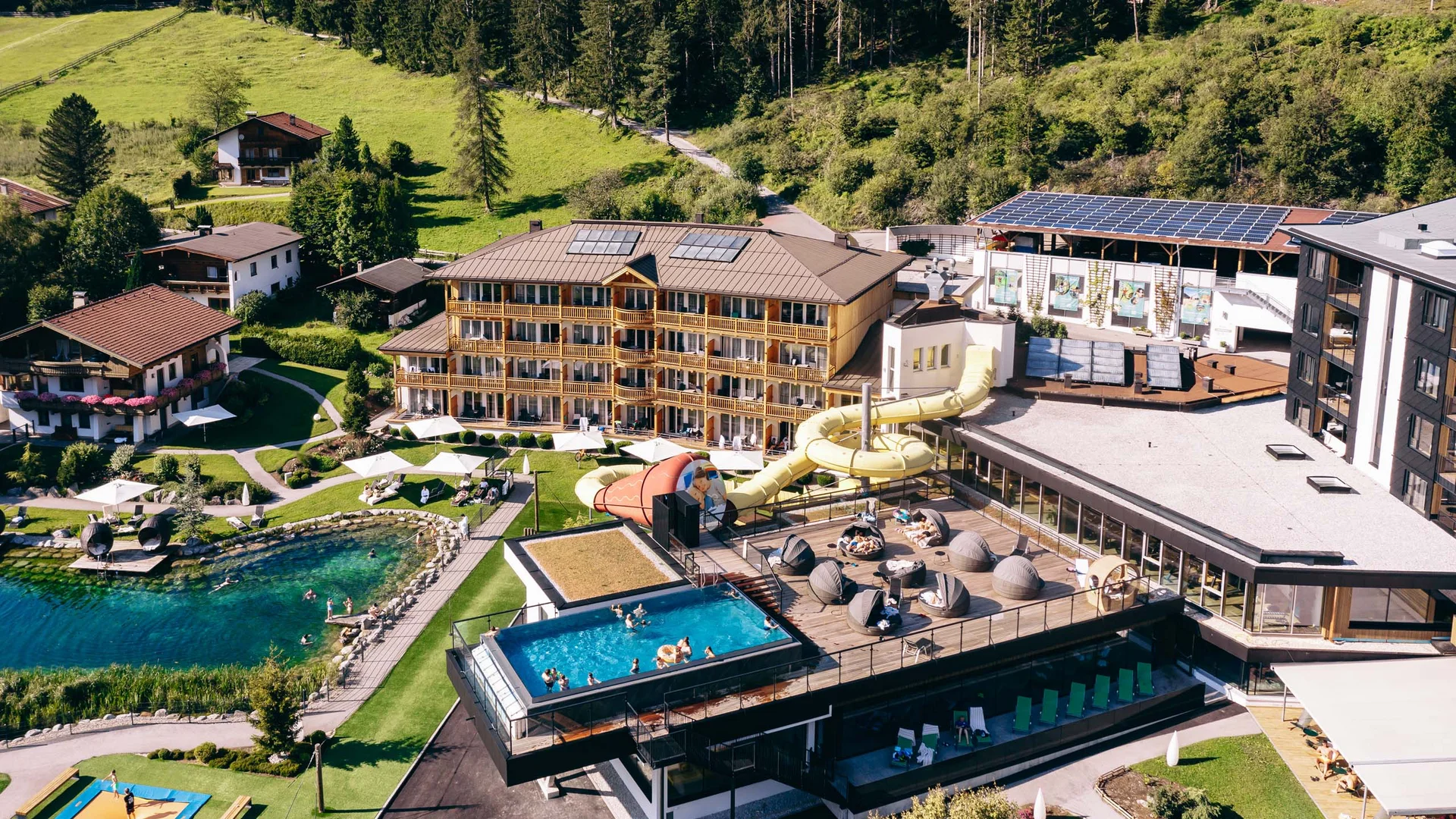 Hotelresort mit Außenpool, Wasserrutsche, Badeteich und Liegebereichen in Berglandschaft