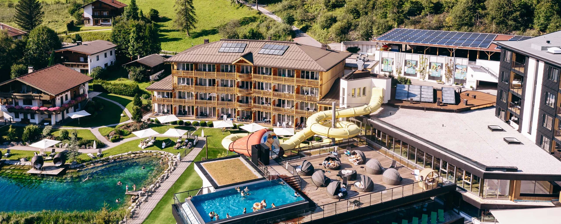 Hotelresort mit Außenpool, Wasserrutsche, Badeteich und Liegebereichen in Berglandschaft