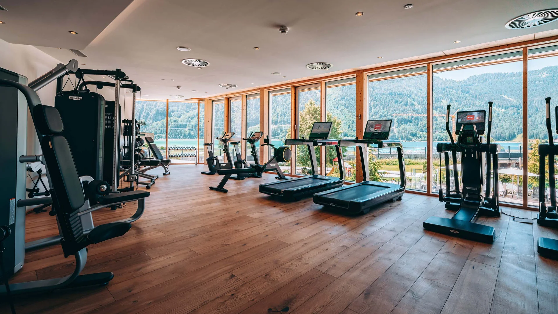 Helles Fitnessstudio mit Geräten und großem Fenster mit Bergblick