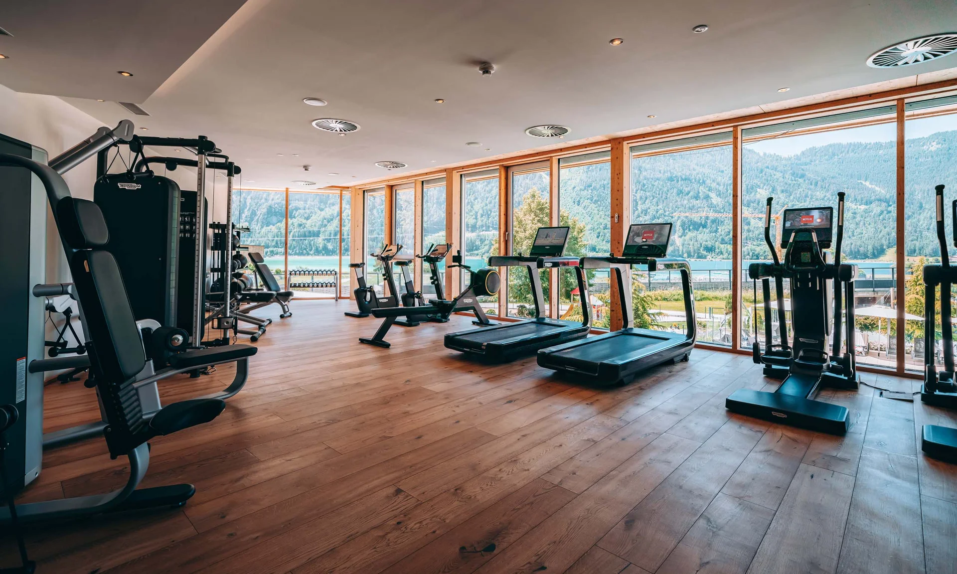 Helles Fitnessstudio mit Geräten und großem Fenster mit Bergblick