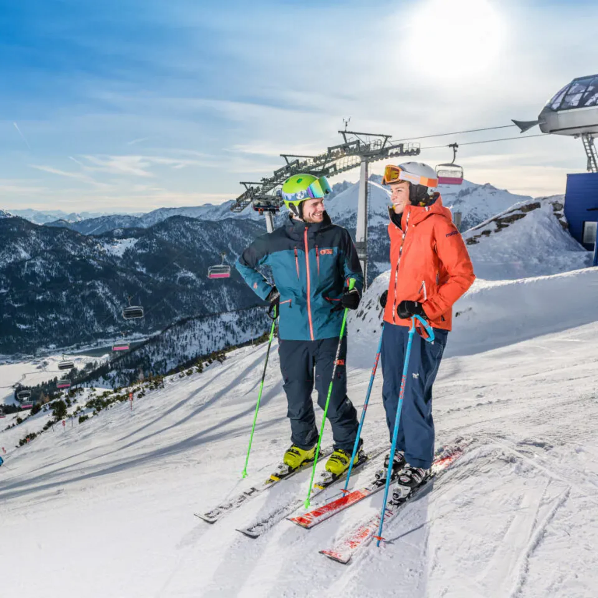Zwei Skifahrer stehen auf verschneiter Piste vor Berglandschaft und Skilift
