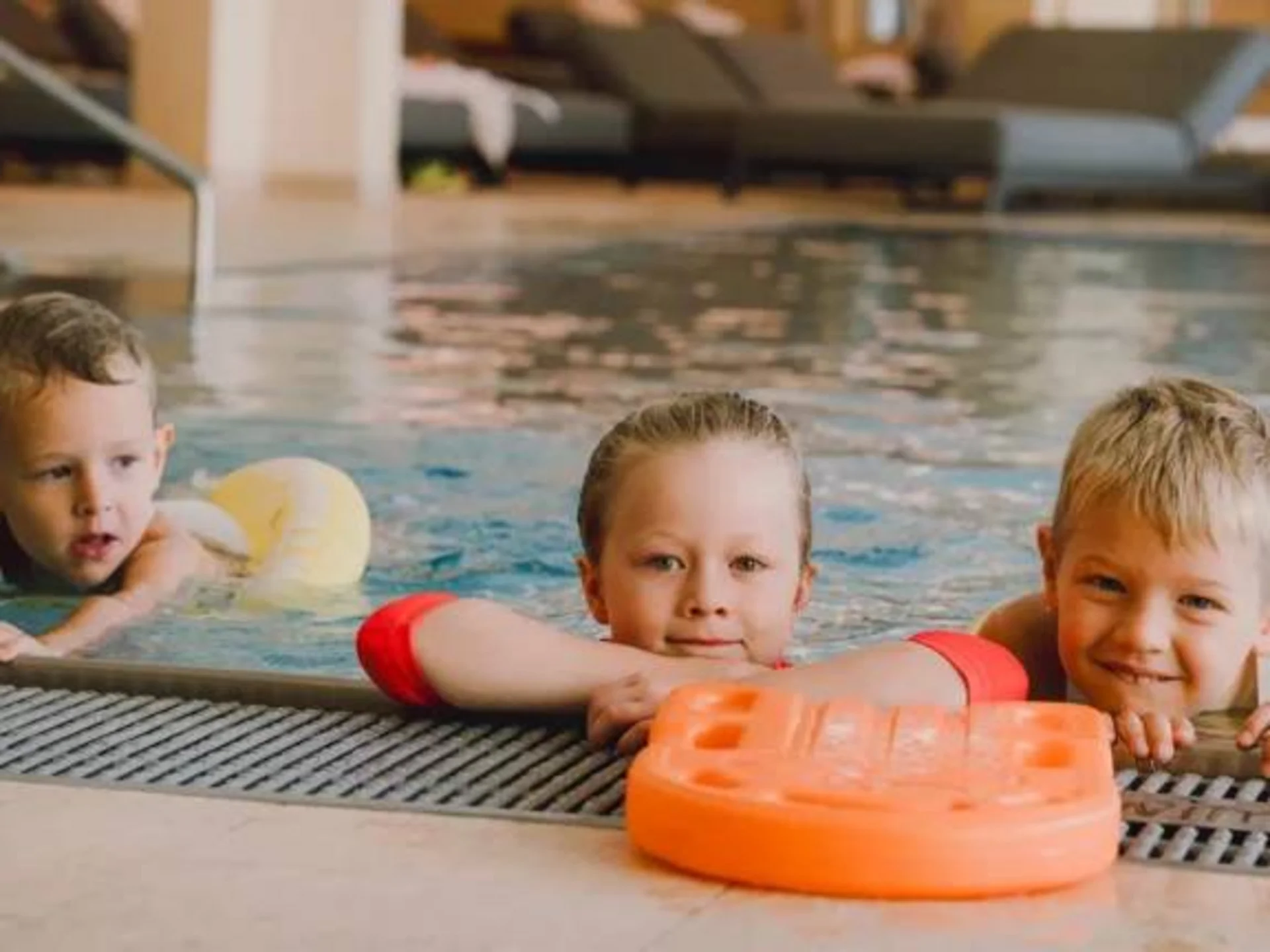 Drei Kinder im Hallenbad am Beckenrand mit Schwimmhilfen