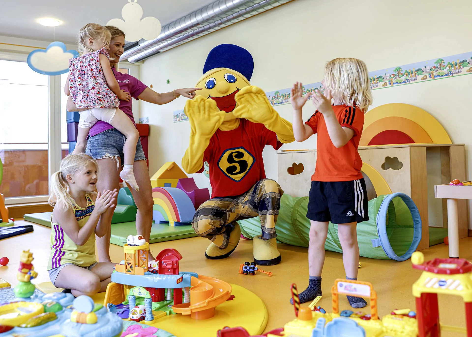 The family resort in Buchau for quality time in Tyrol Children playing and clapping with a person in a colorful mascot costume in a playroom