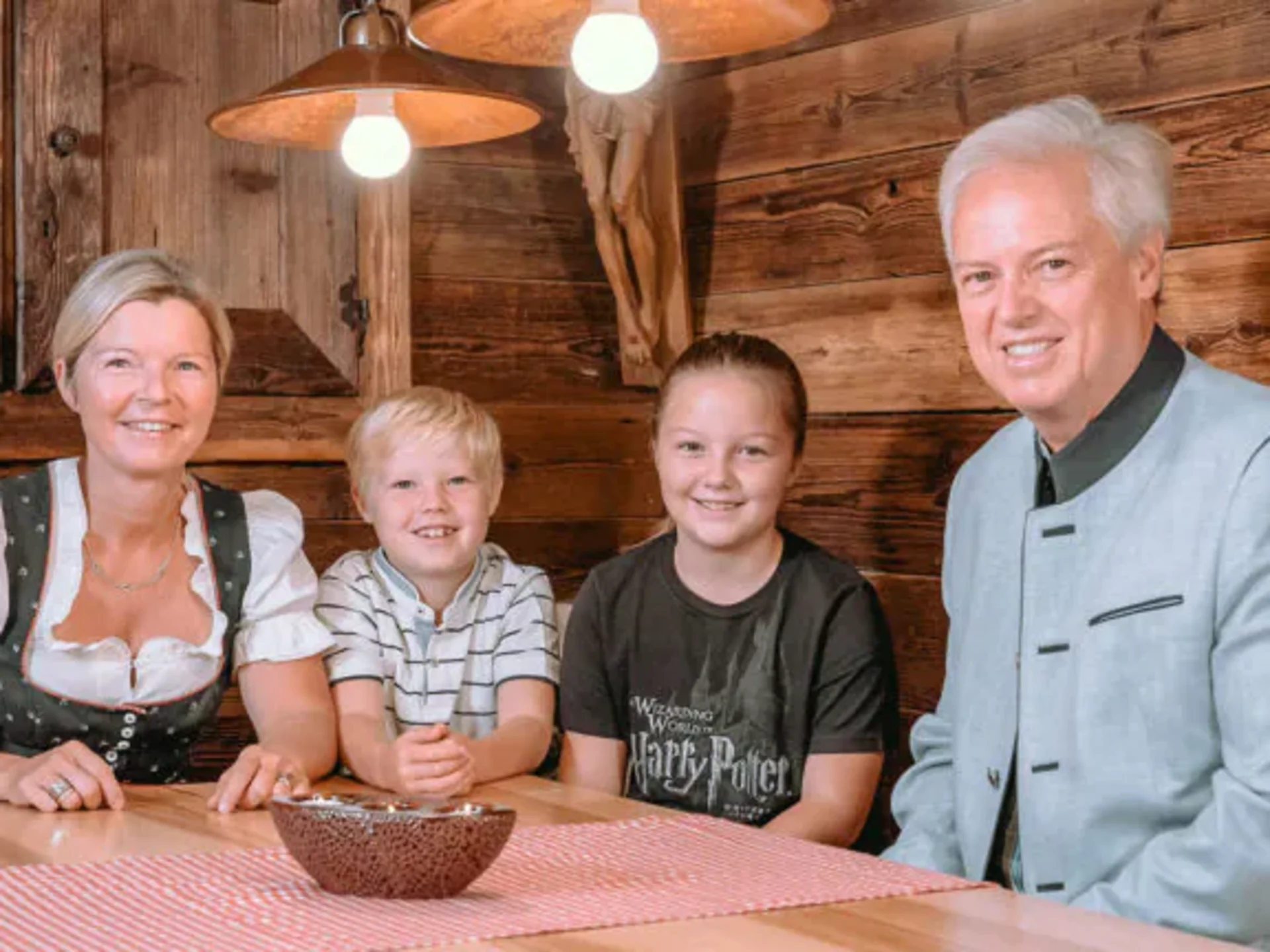 Familie sitzt an Holztisch in traditionellem Raum mit Hängelampen