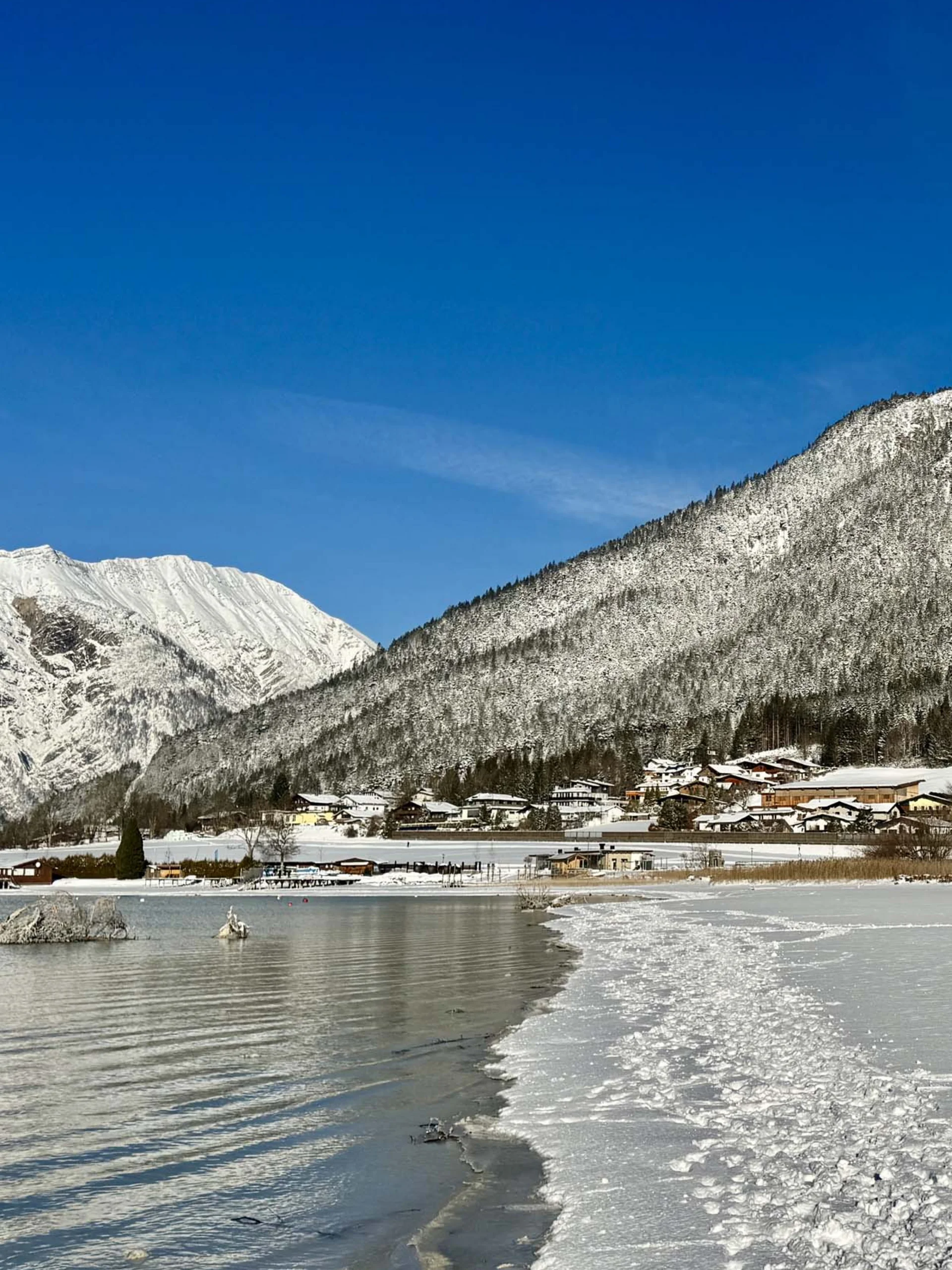 Verschneite Berglandschaft mit Dorf am gefrorenen See unter klarem blauen Himmel