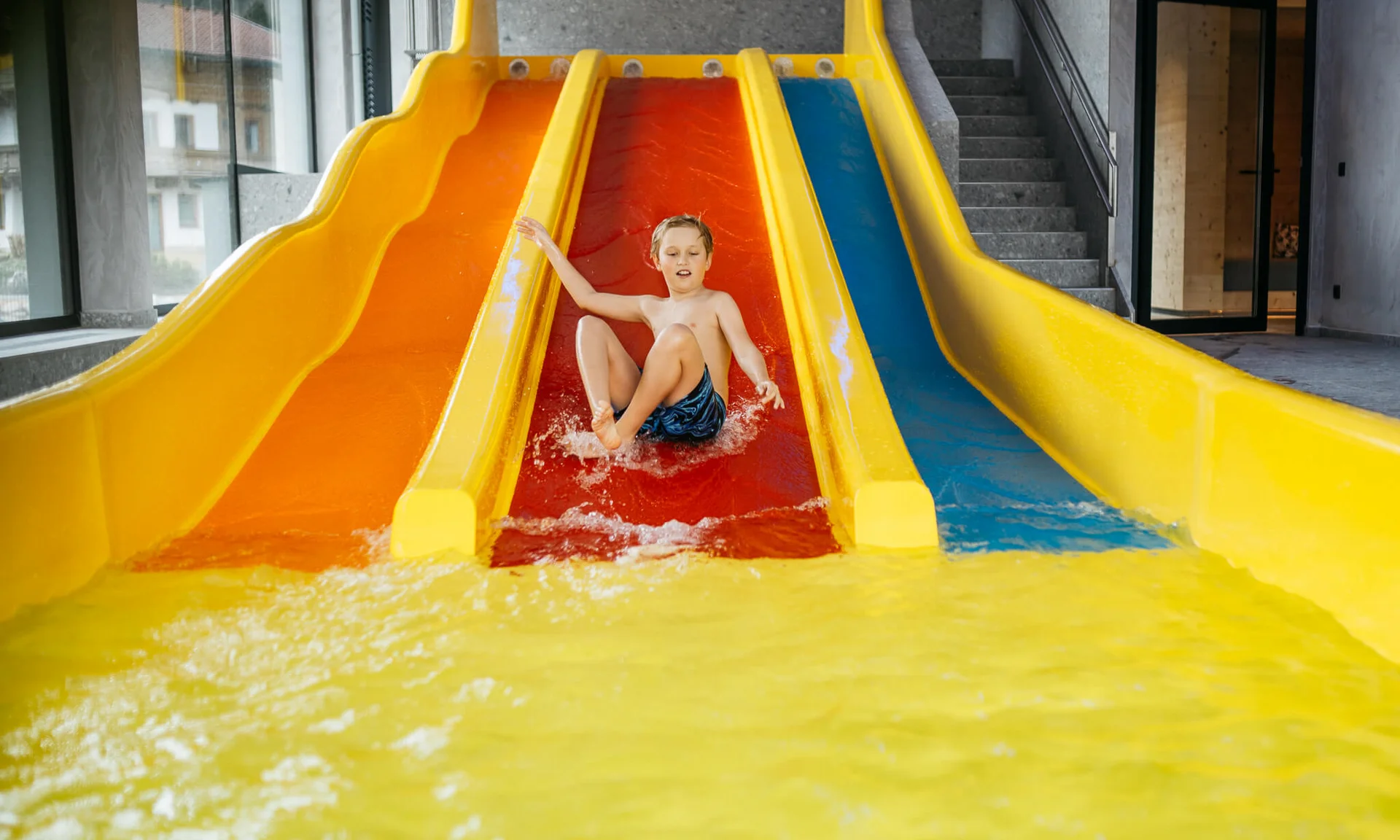 Kind rutscht auf roter Wasserrutsche in Hallenbad ins Wasser