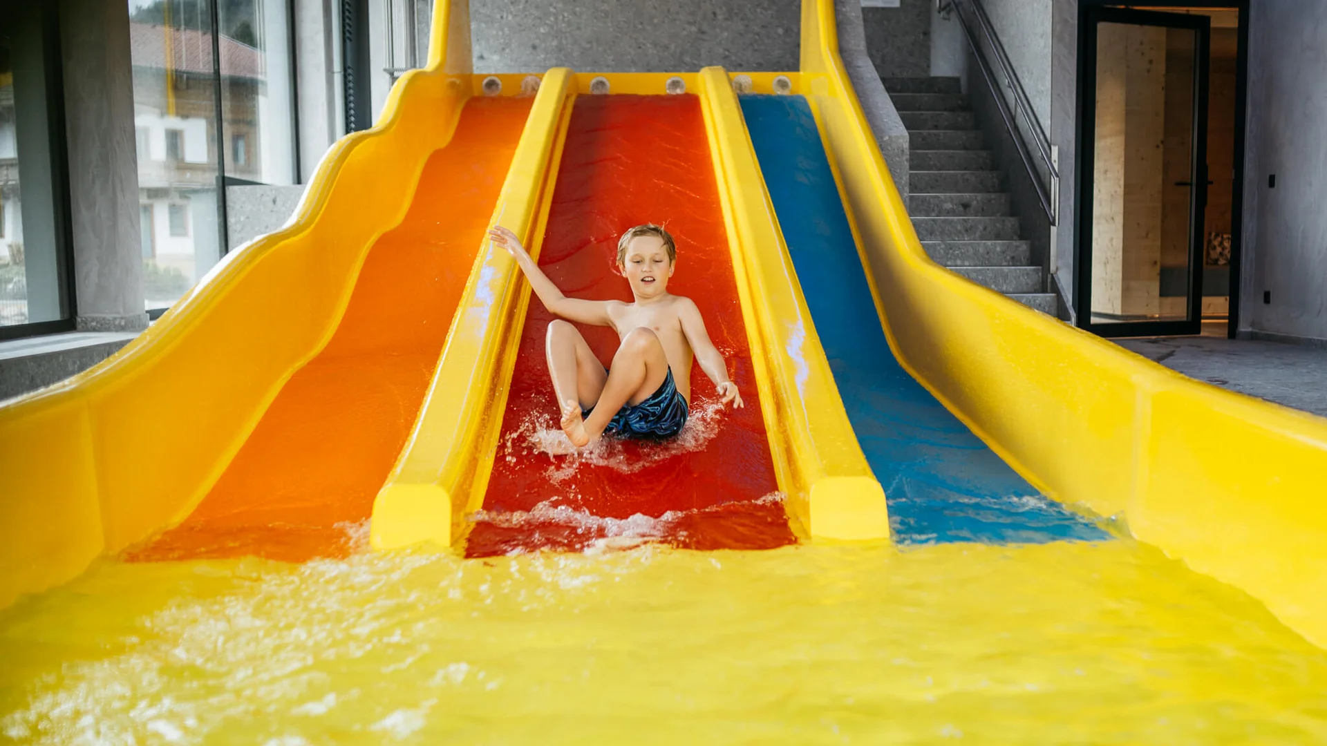 Kind rutscht auf roter Wasserrutsche in Hallenbad ins Wasser