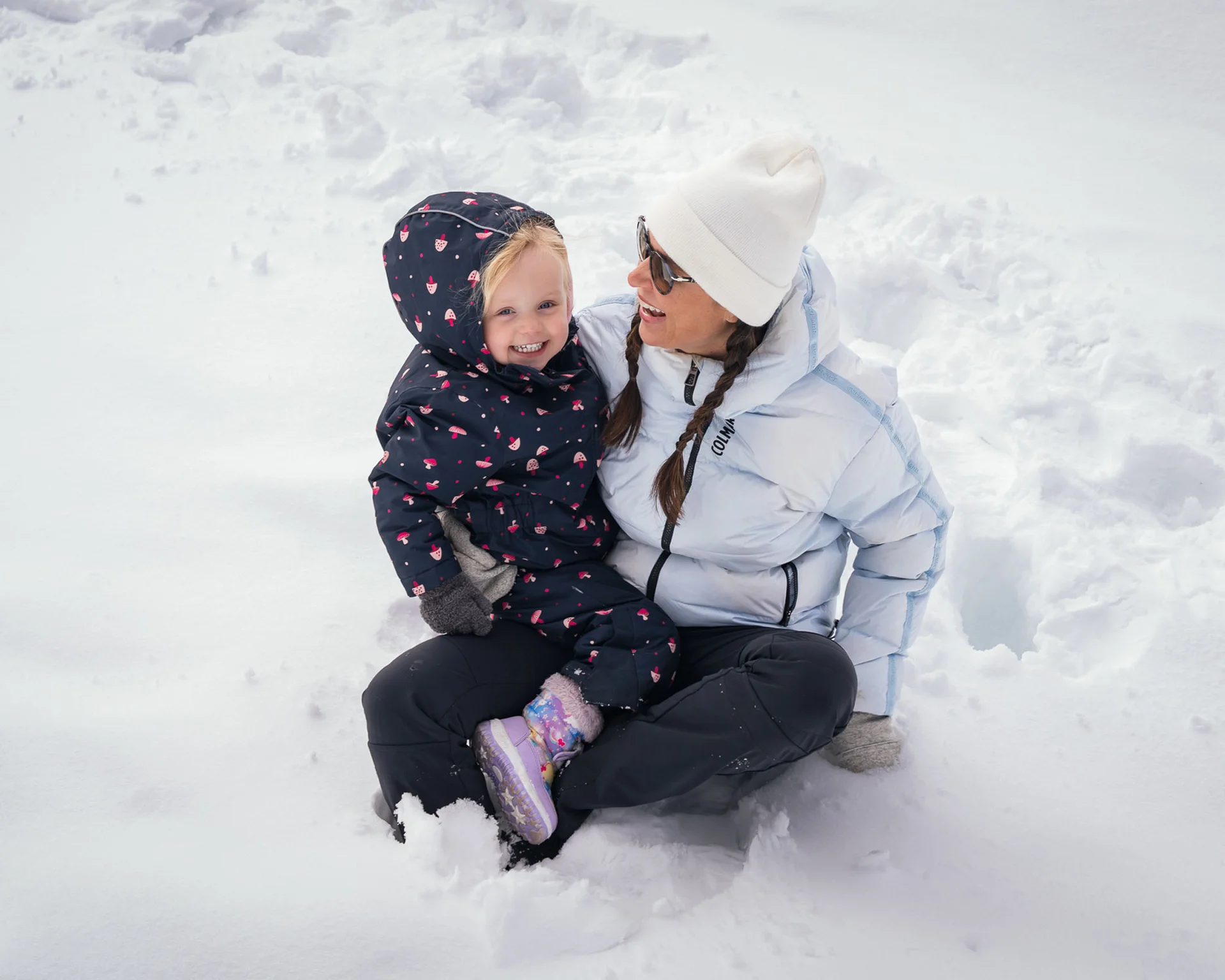 Mutter und Kind lachen im Schnee, beide warm angezogen