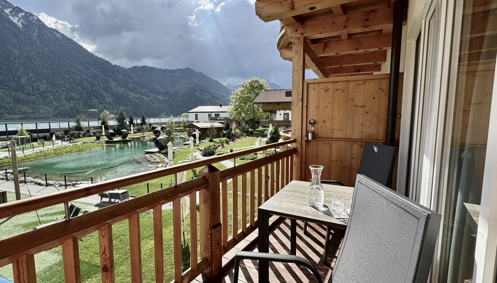 Balkon mit Stühlen und Tisch mit Berg- und Teichblick bei bewölktem Himmel