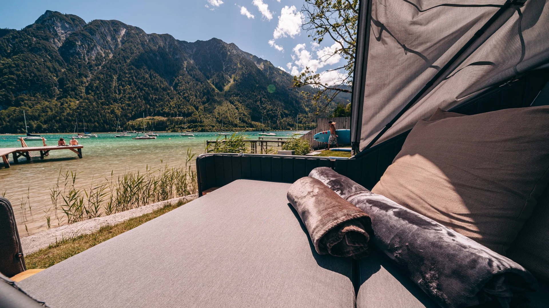 Liegesofa mit Decken am See mit Bergblick und Booten bei sonnigem Wetter