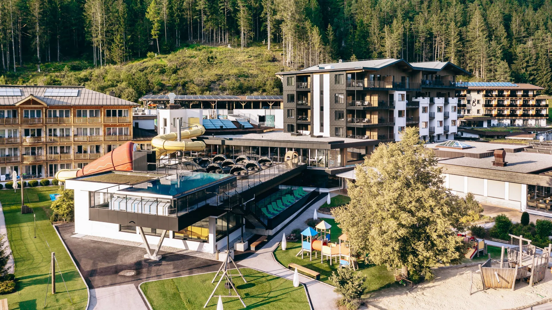 Moderner Hotelkomplex mit Wasserrutschen, Spielplatz und Wald im Hintergrund