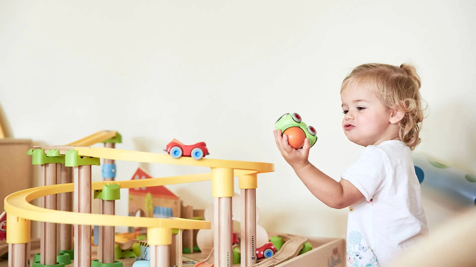 Kleines Kind spielt mit einer Holzeisenbahn und Spielsachen zu Hause.