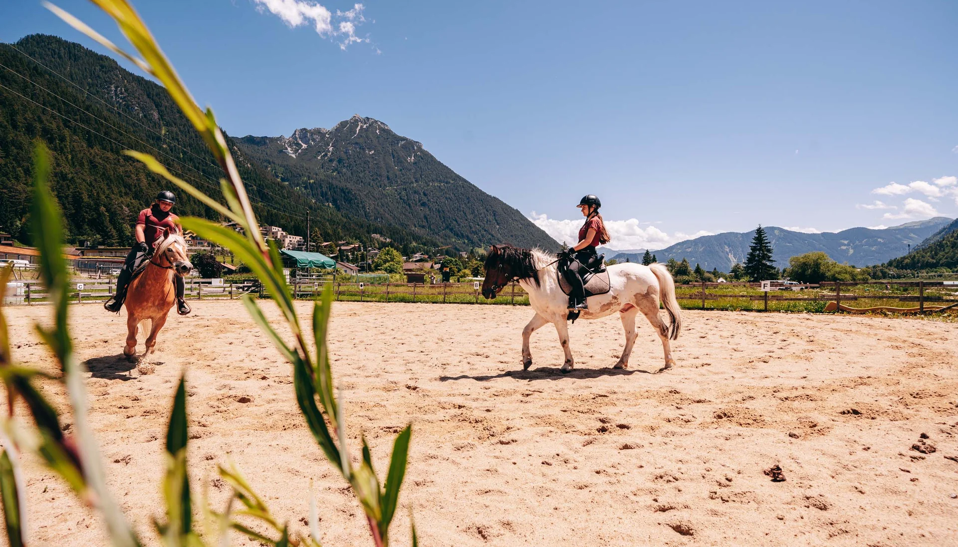 Zwei Reiter auf Pferden auf einem Sandplatz mit Bergen im Hintergrund