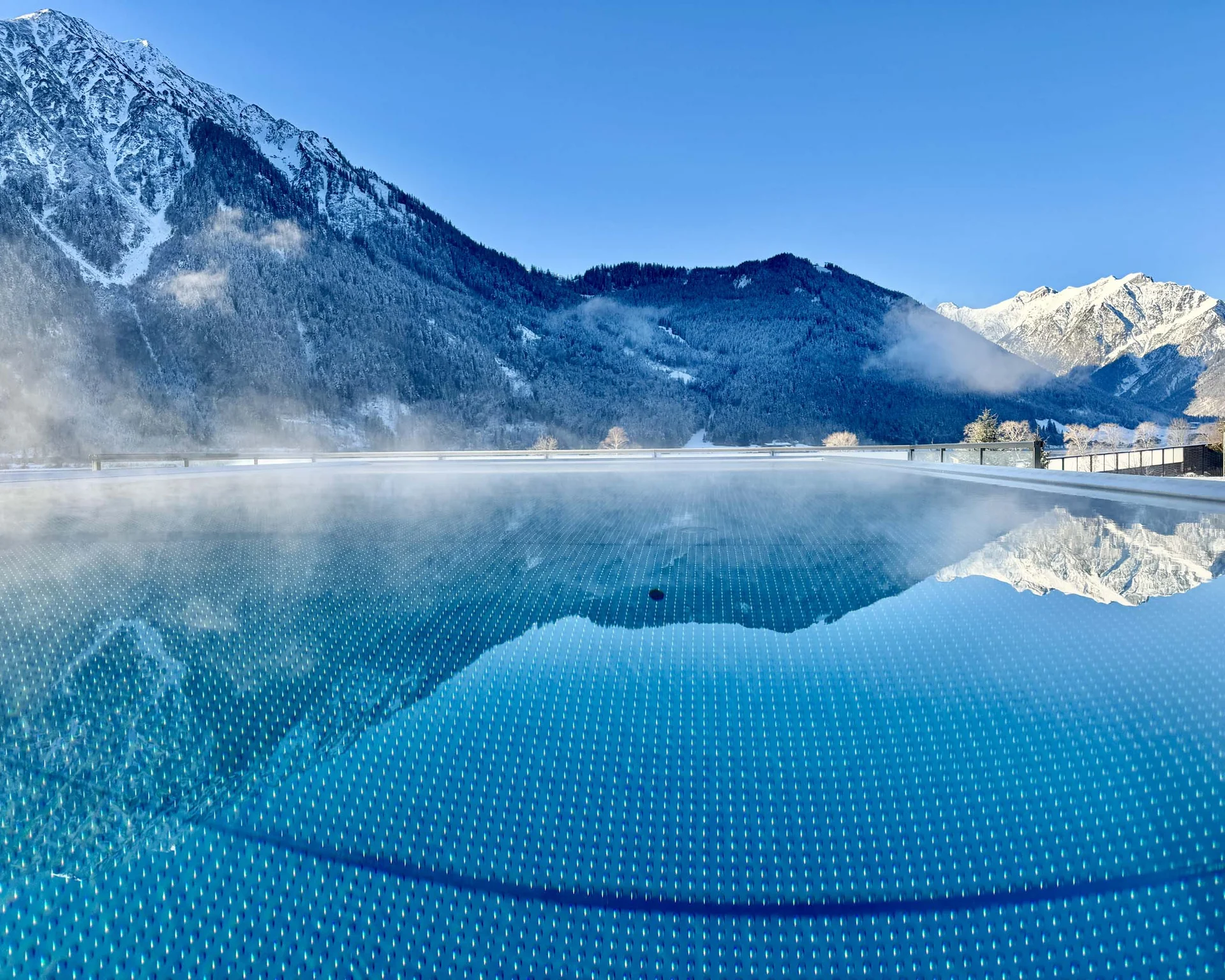Erholungsurlaub für Eltern Dampfender Pool mit Spiegelung schneebedeckter Berge im Hintergrund