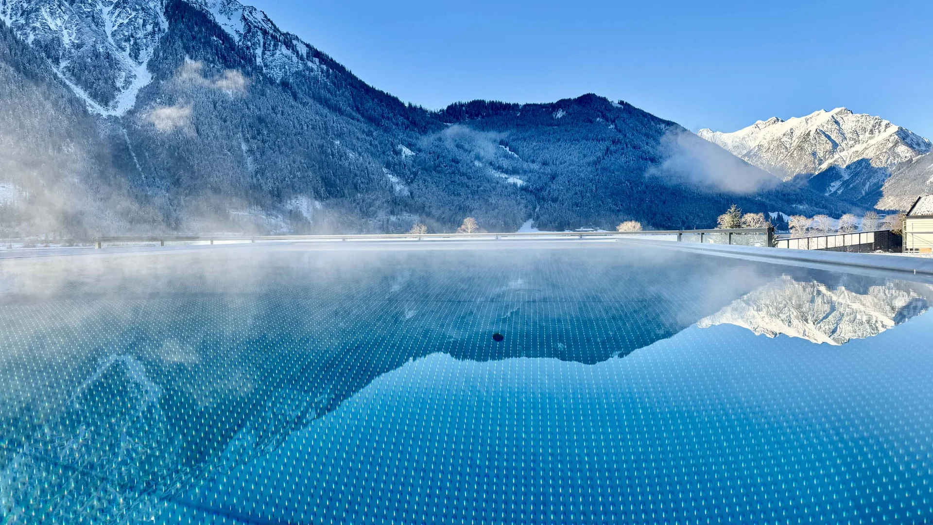 Dampfender Pool mit Spiegelung schneebedeckter Berge im Hintergrund