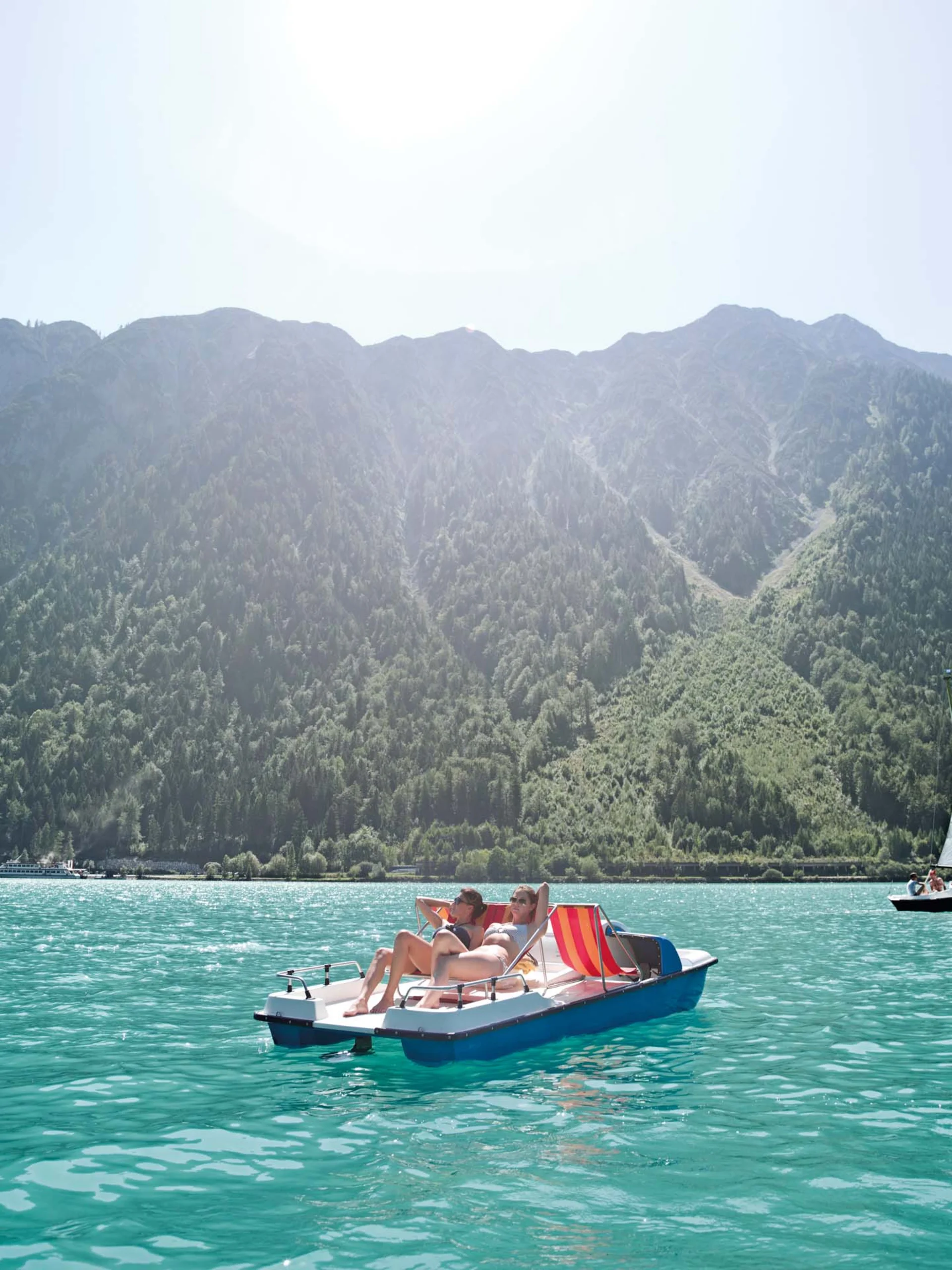 Zwei Personen entspannen auf einem Tretboot auf dem türkisfarbenen See vor Bergen