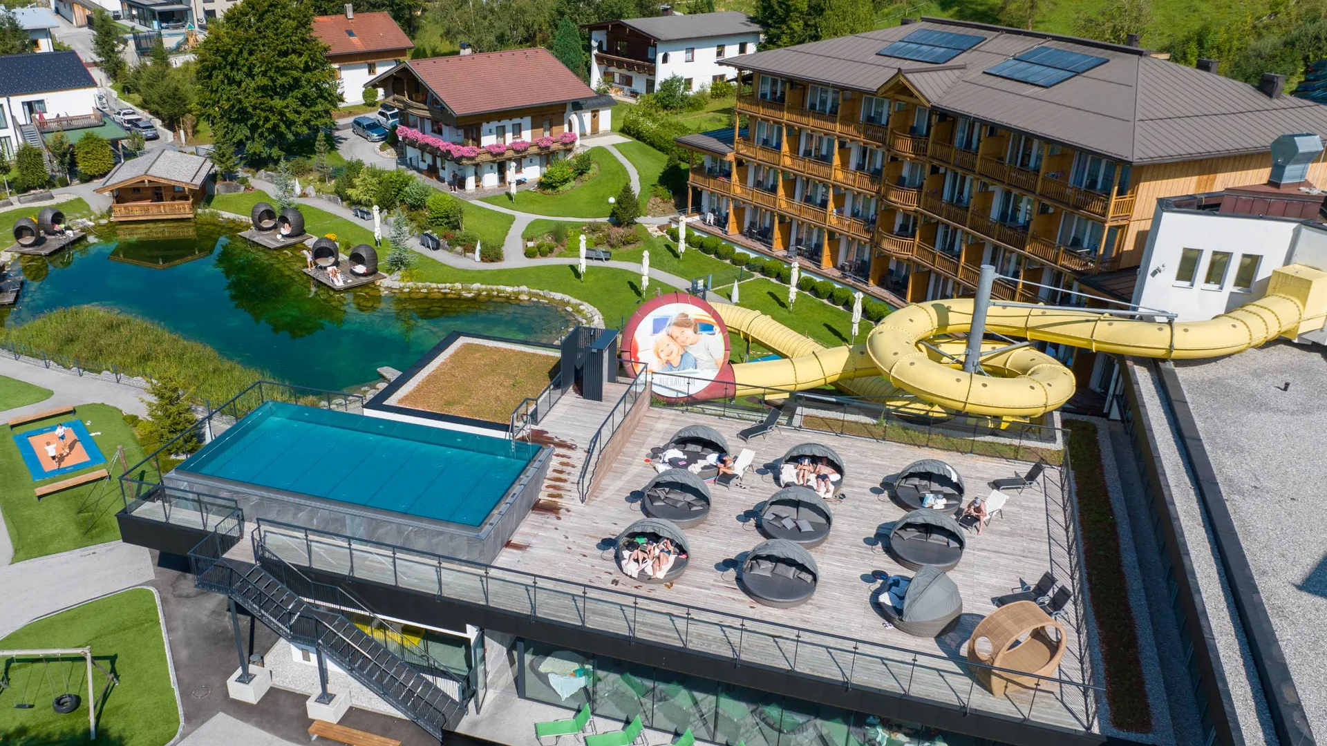 Luftaufnahme eines Hotels mit Liegefläche, Wasserrutsche und Teich im Garten