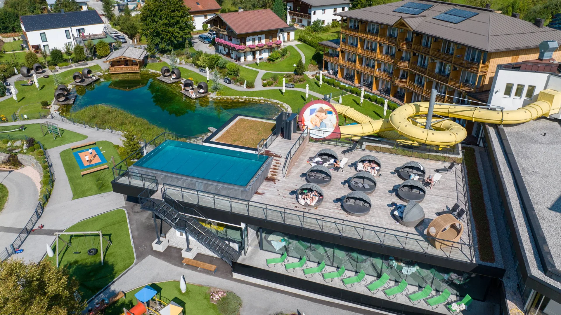 Luftaufnahme eines Hotels mit Liegefläche, Wasserrutsche und Teich im Garten