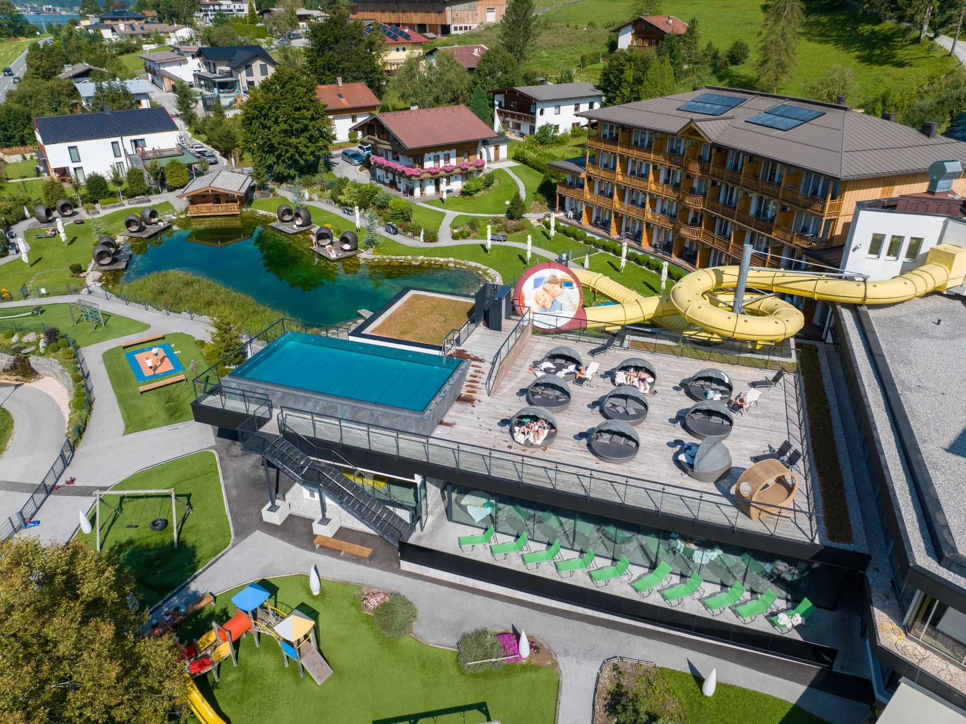 Luftaufnahme eines Hotels mit Liegefläche, Wasserrutsche und Teich im Garten
