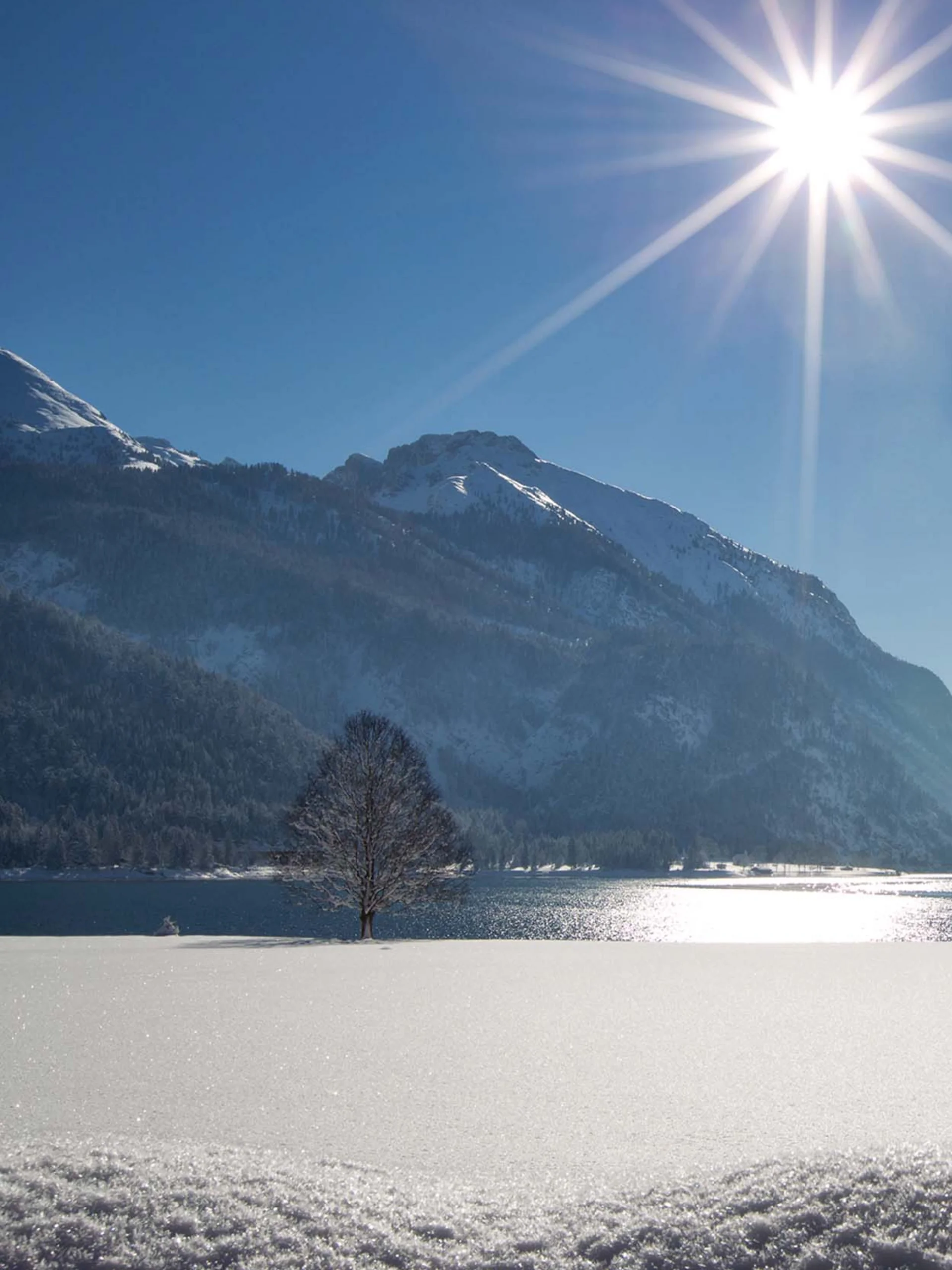 Schneebedeckter Bergsee bei Sonnenschein mit Bergen und blauem Himmel