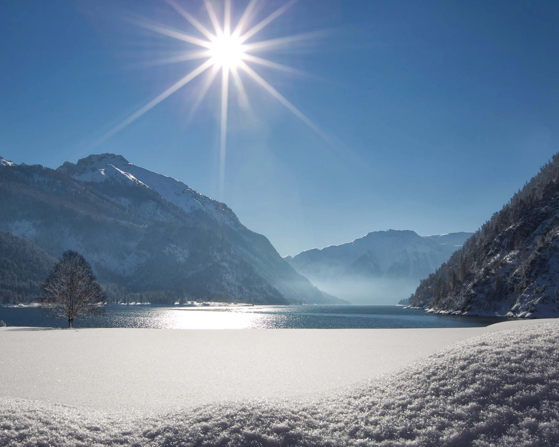 Schneebedeckter Bergsee bei Sonnenschein mit Bergen und blauem Himmel
