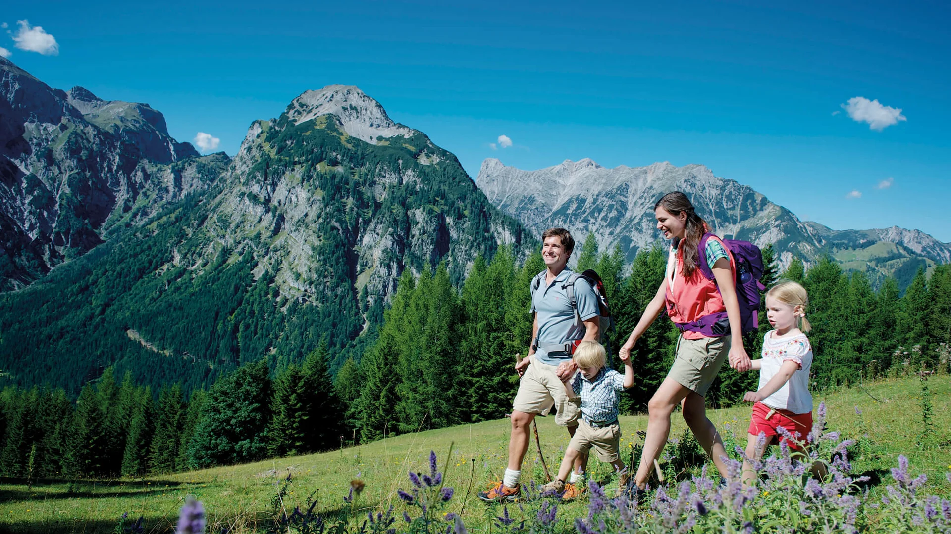 Familie wandert in den Bergen bei sonnigem Wetter mit blühender Wiese