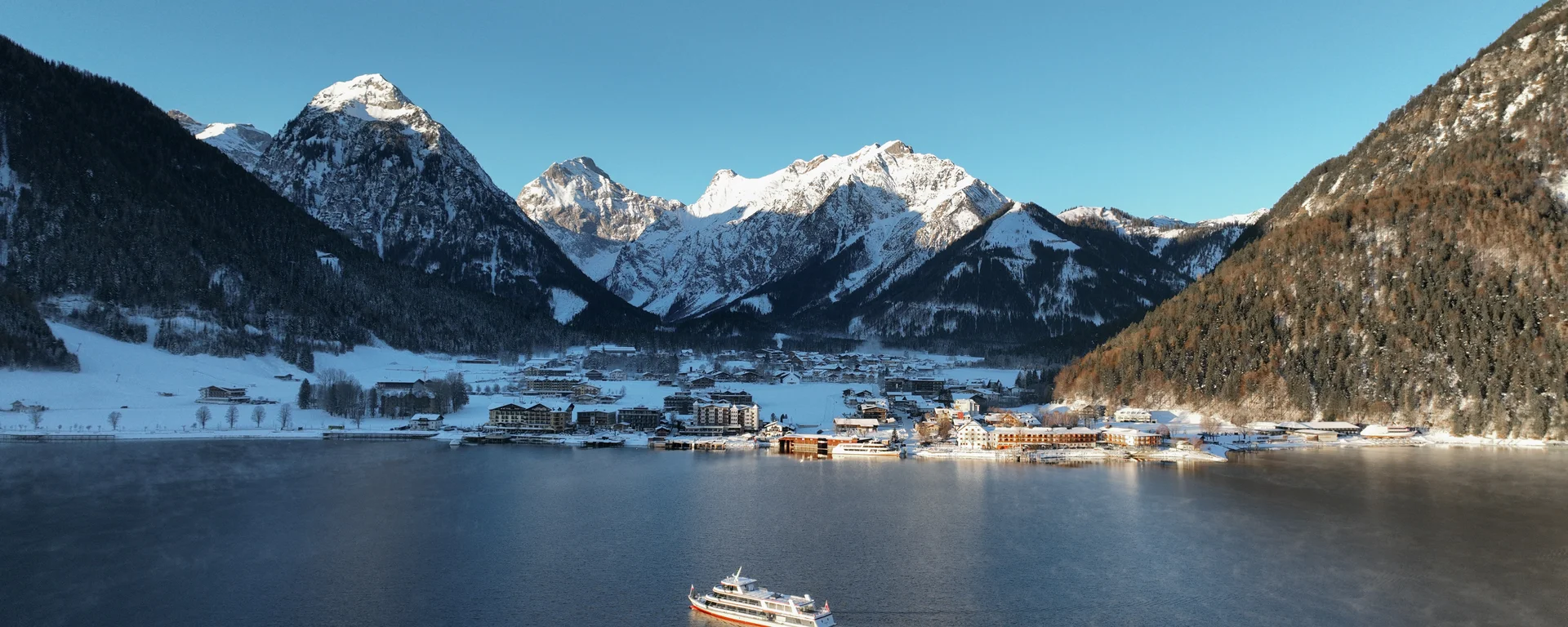 Sehenswertes rund um Eben am Achensee Schiff auf See vor schneebedecktem Bergdorf in klarer Winterlandschaft