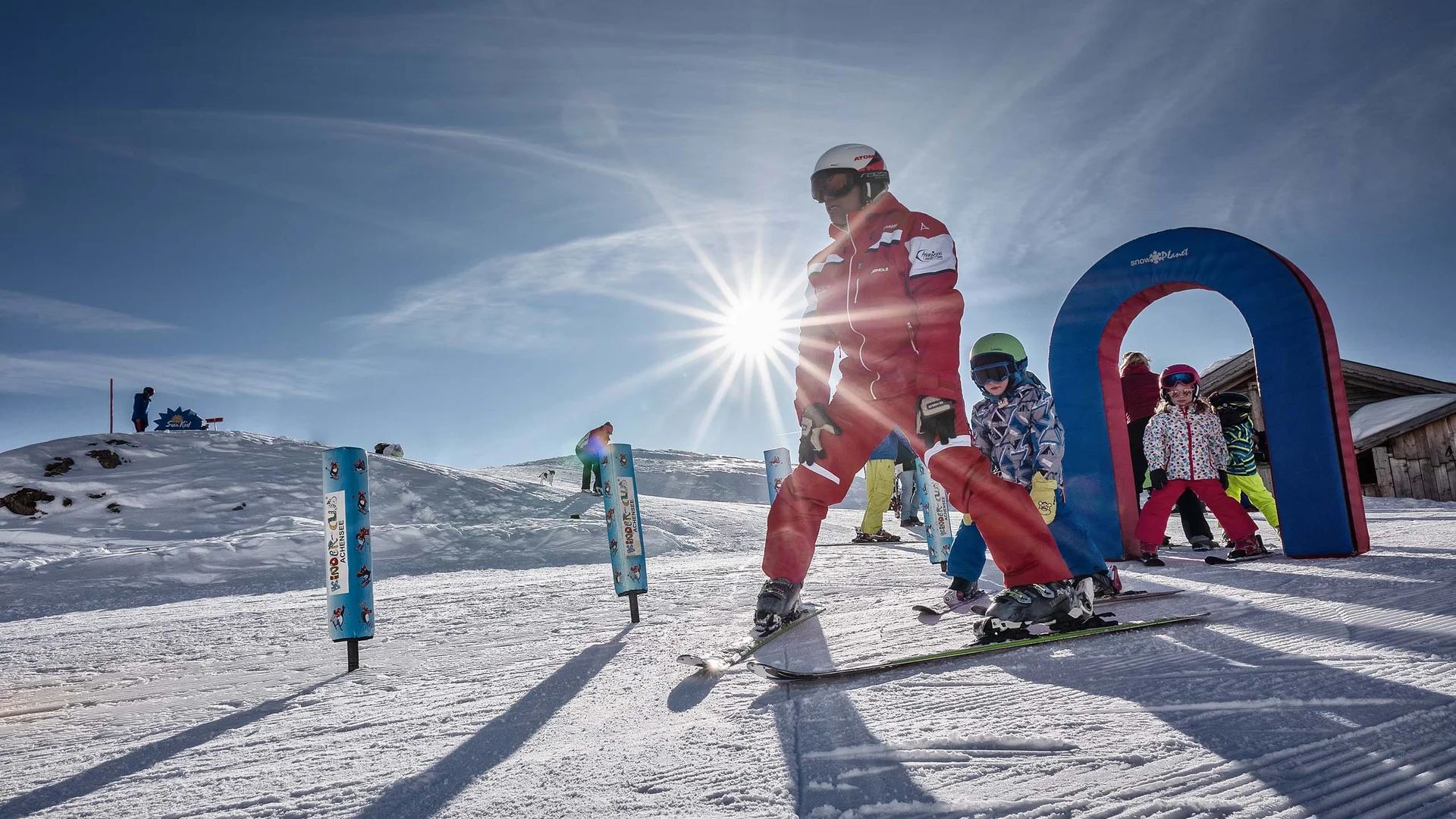 Skilehrer mit Kindern beim Skikurs im Schnee an einem sonnigen Tag
