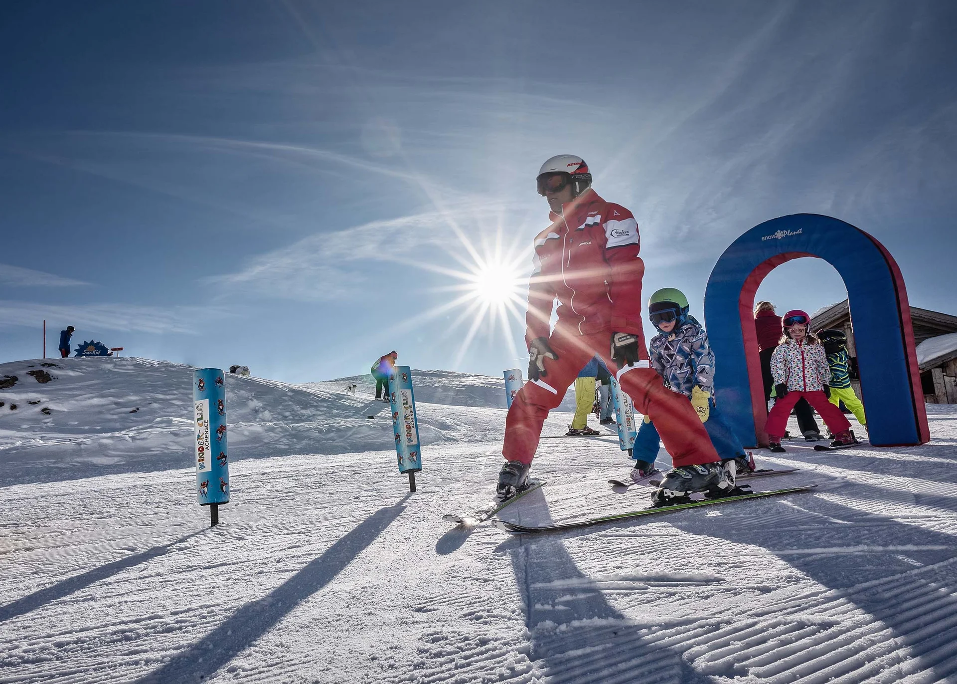 Become a regular guest and collect Buchau Tokens Ski instructor teaching children skiing on snowy slope under bright sun