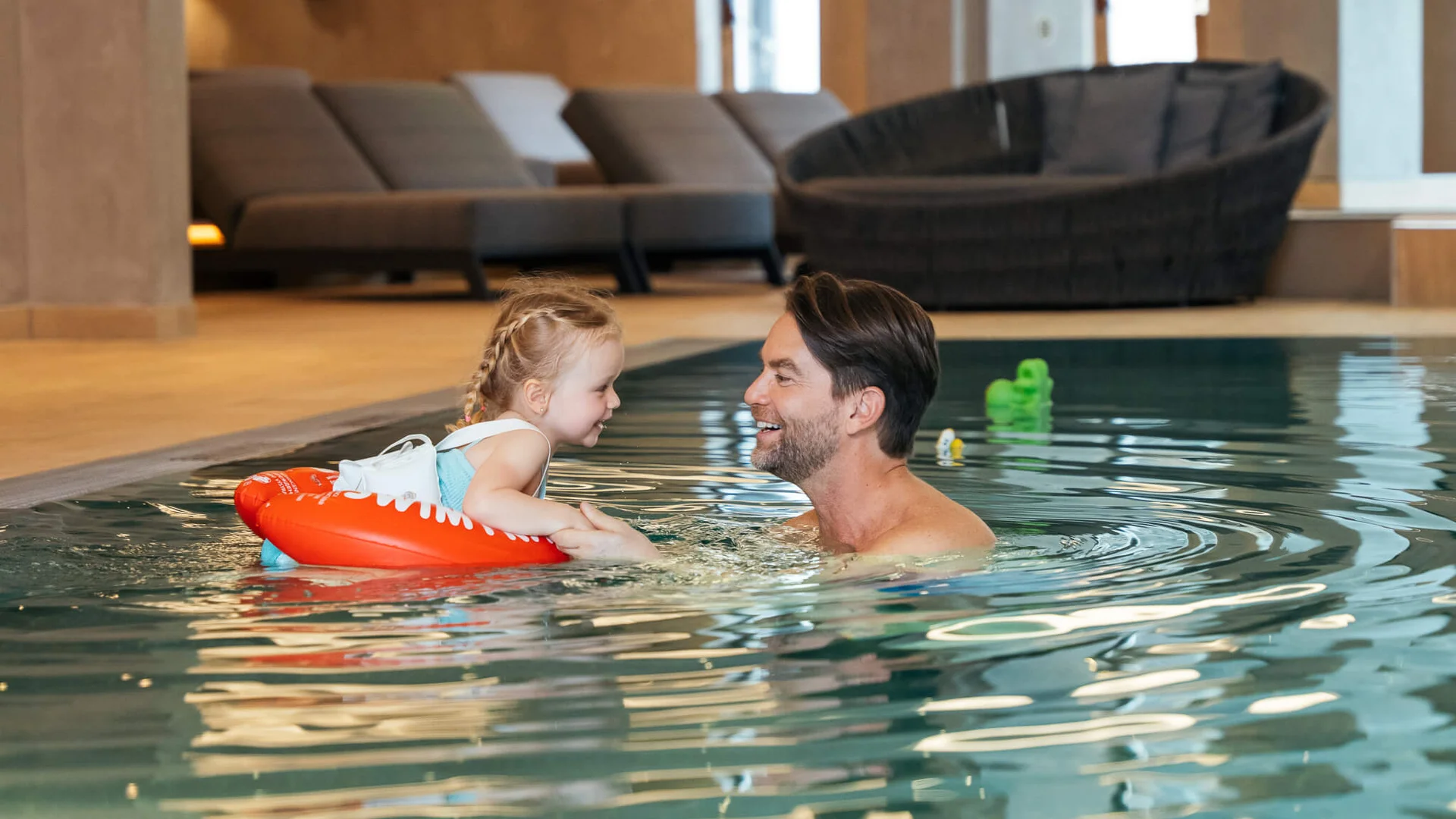 Mann und Kind mit Schwimmring lächelnd und Händchen haltend im Hallenbad
