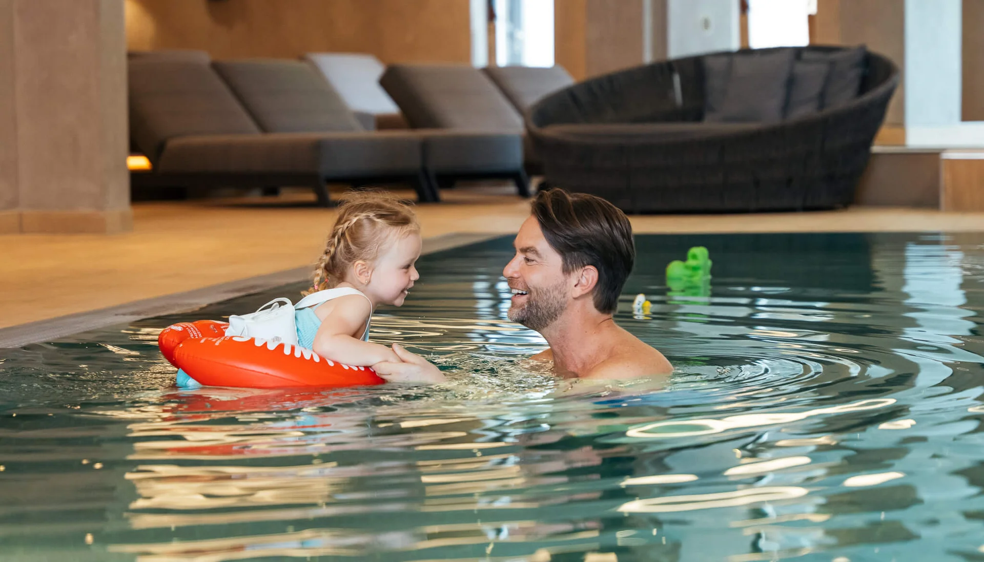 Mann und Kind mit Schwimmring lächelnd und Händchen haltend im Hallenbad