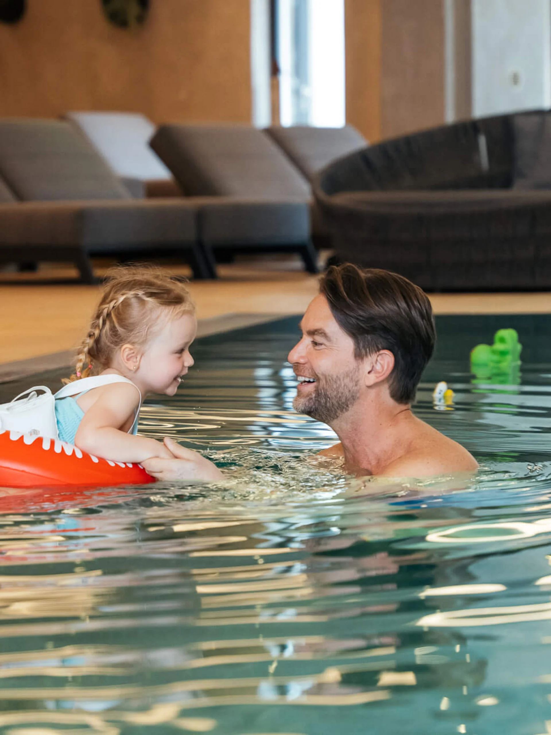 Mann und Kind mit Schwimmring lächelnd und Händchen haltend im Hallenbad